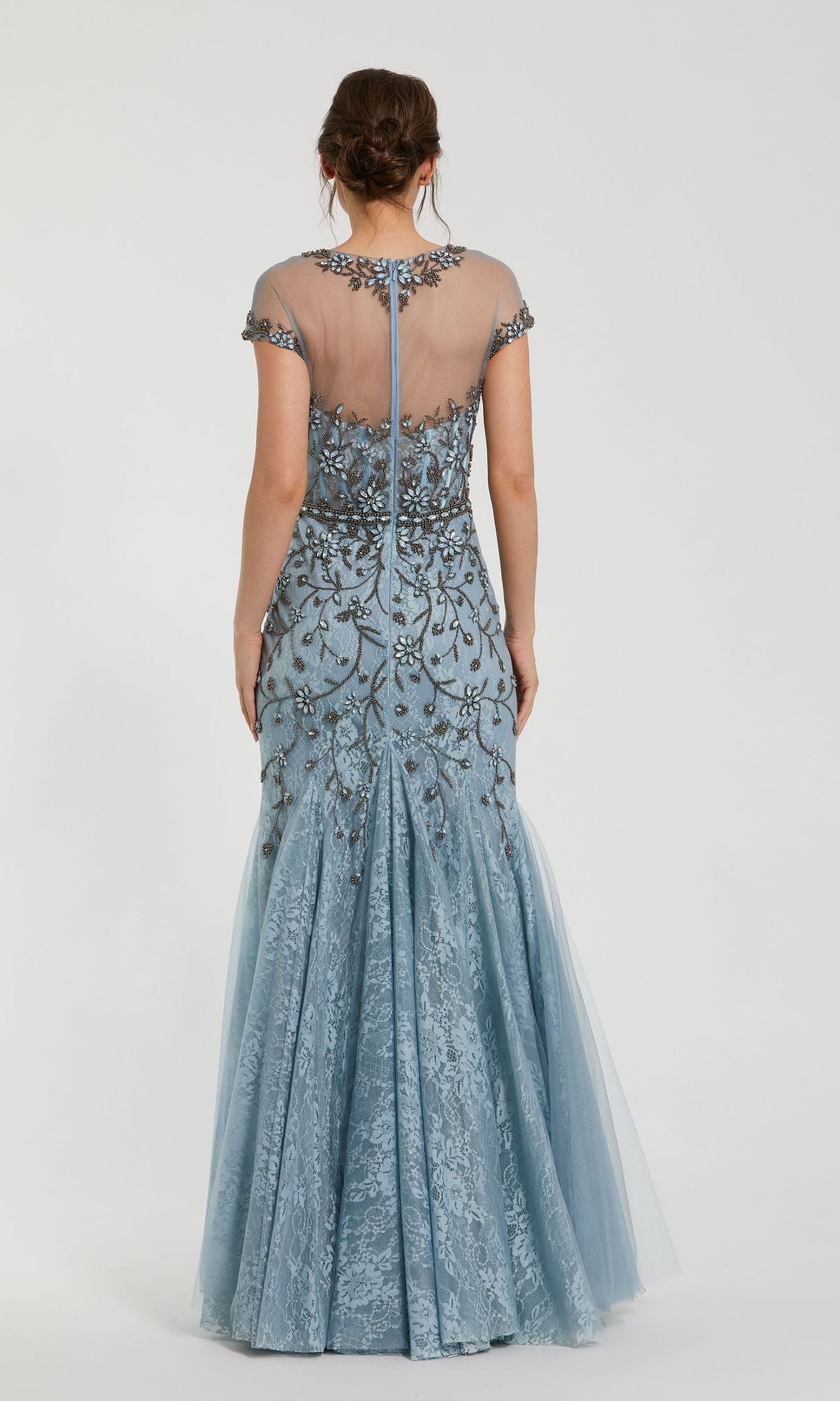 A woman faces away, wearing the Beaded Long Blue Formal Dress: Mac Duggal 2239—a floor-length gown with lace, tulle, floral embroidery, cap sleeves, and a sheer back panel with a central zipper.