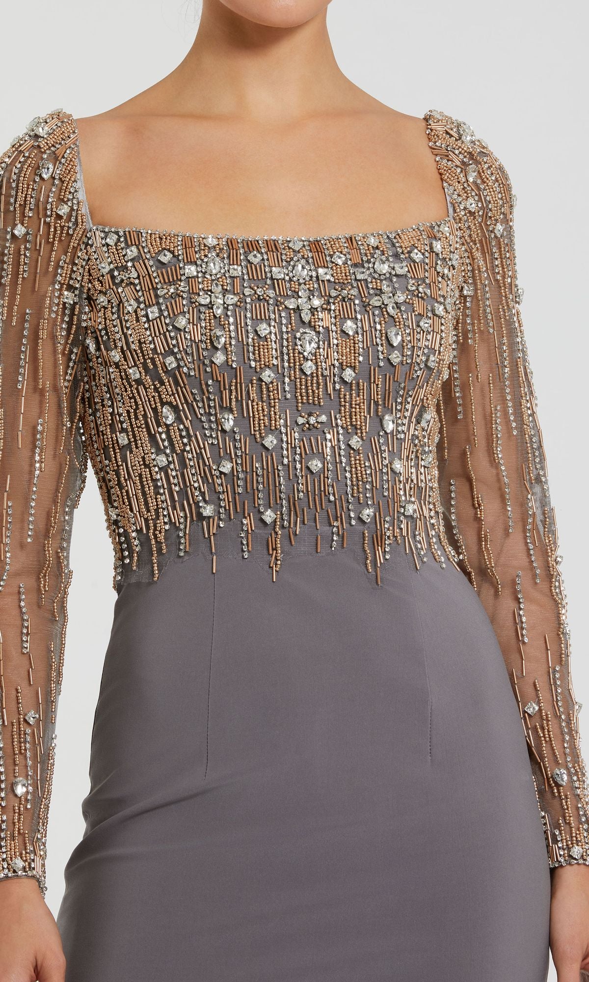 A person wearing the Mac Duggal 2256 Long Sleeve Long Formal Dress, featuring a square neckline, sheer beaded sleeves and bodice with metallic and crystal accents, paired with a fitted gray skirt.