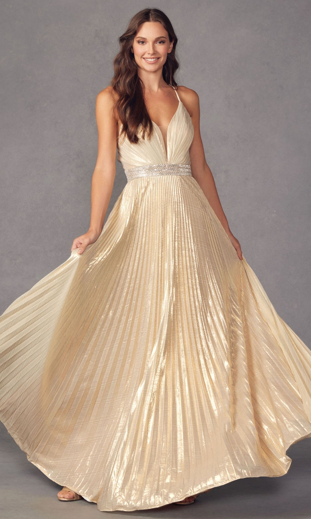 Woman wearing the Deep V-Neck Pleated Long A-Line Prom Dress 226, a sleeveless gold floor-length gown with a deep V-neck, fitted waistband, and rhinestone belt, standing against a plain gray background.