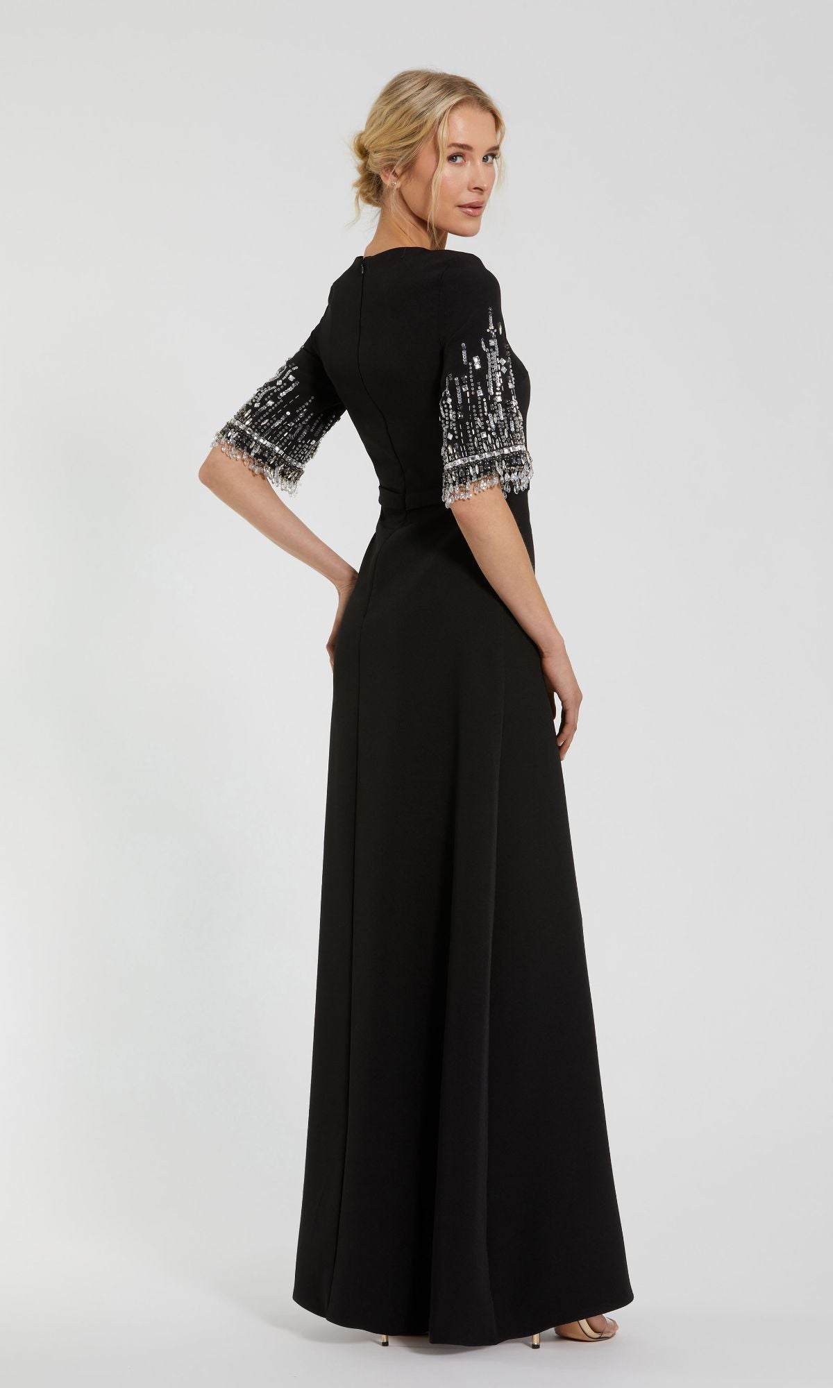 A woman stands sideways, looking over her shoulder, wearing the Mac Duggal 2270 Short Sleeve Sleek Formal Dress with sequin-embellished sleeves against a plain background.