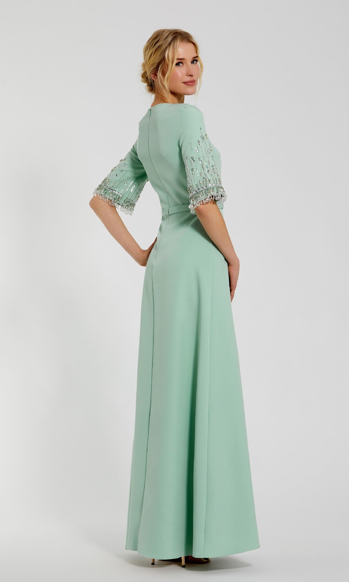 Woman posing in the Mac Duggal 2270 Short Sleeve Sleek Formal Dress, featuring light green fabric and embellished sleeves, standing slightly turned against a plain background.
