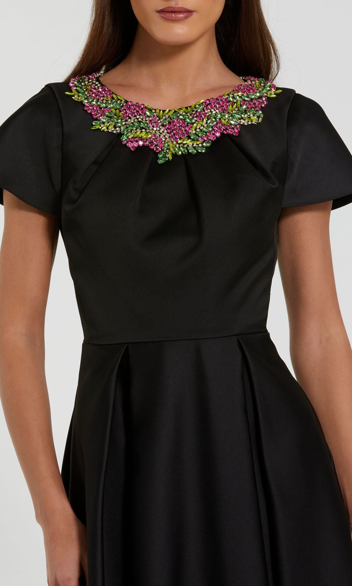 A woman wears the Mac Duggal 2272 short sleeve black formal dress, featuring pink and green beaded floral embellishments at the neckline.