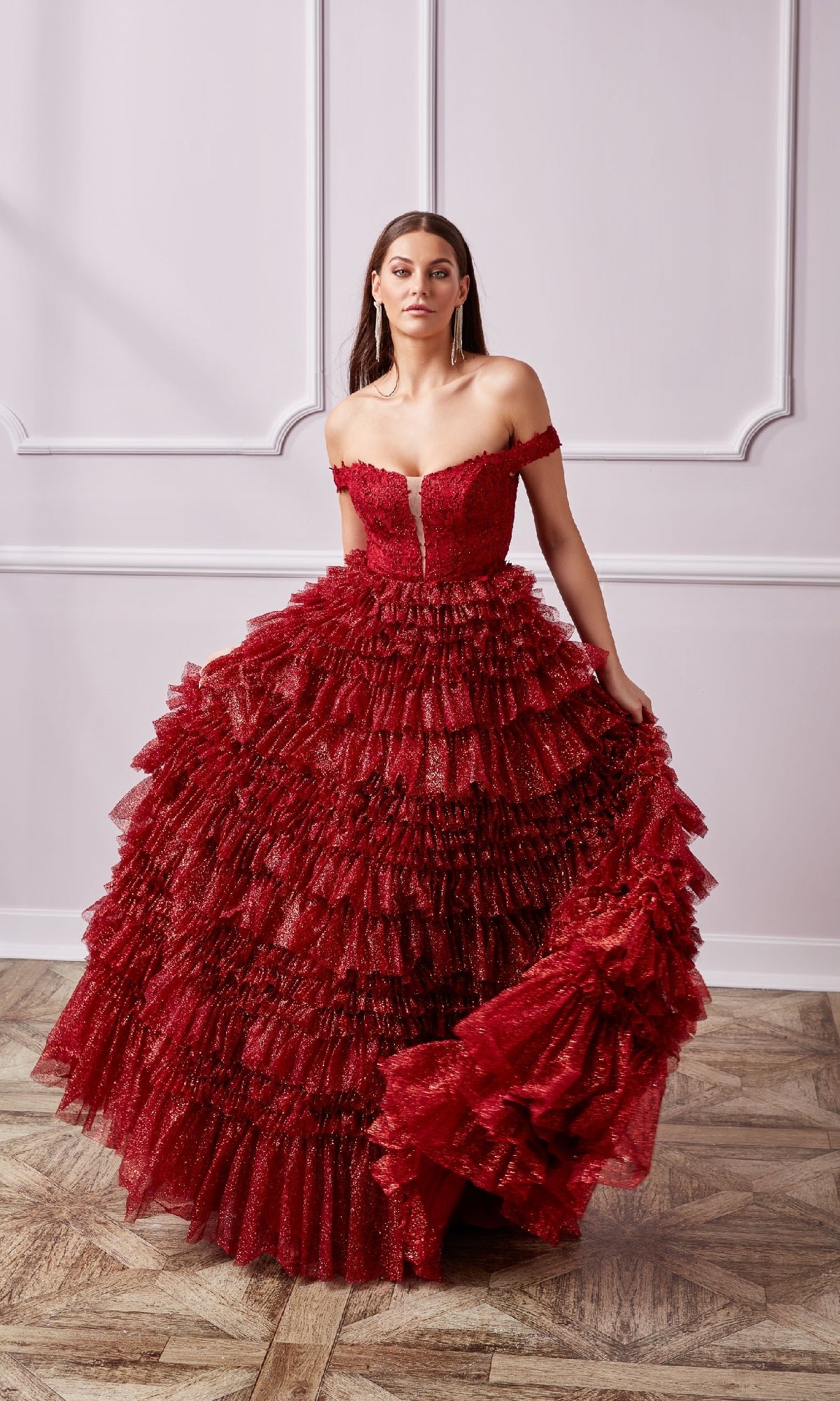 A woman stands in a decorated room with pale walls and wooden flooring, wearing a Lace-Up Long A-Line Glitter Prom Dress with ruffles.