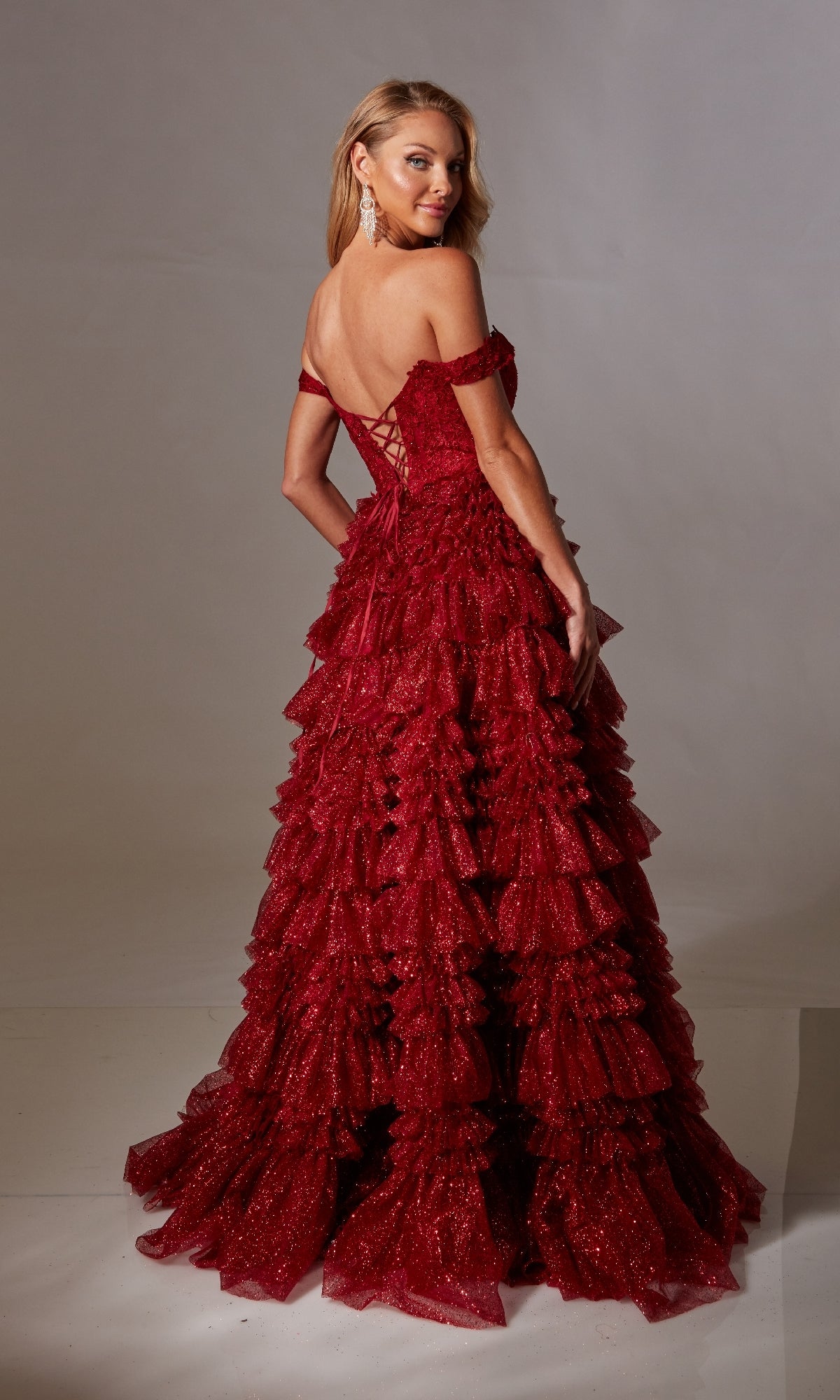 A woman models the Lace-Up Long A-Line Glitter Prom Dress with Ruffles, featuring a red off-shoulder design and elegant lace-up back—perfect for formal occasions.