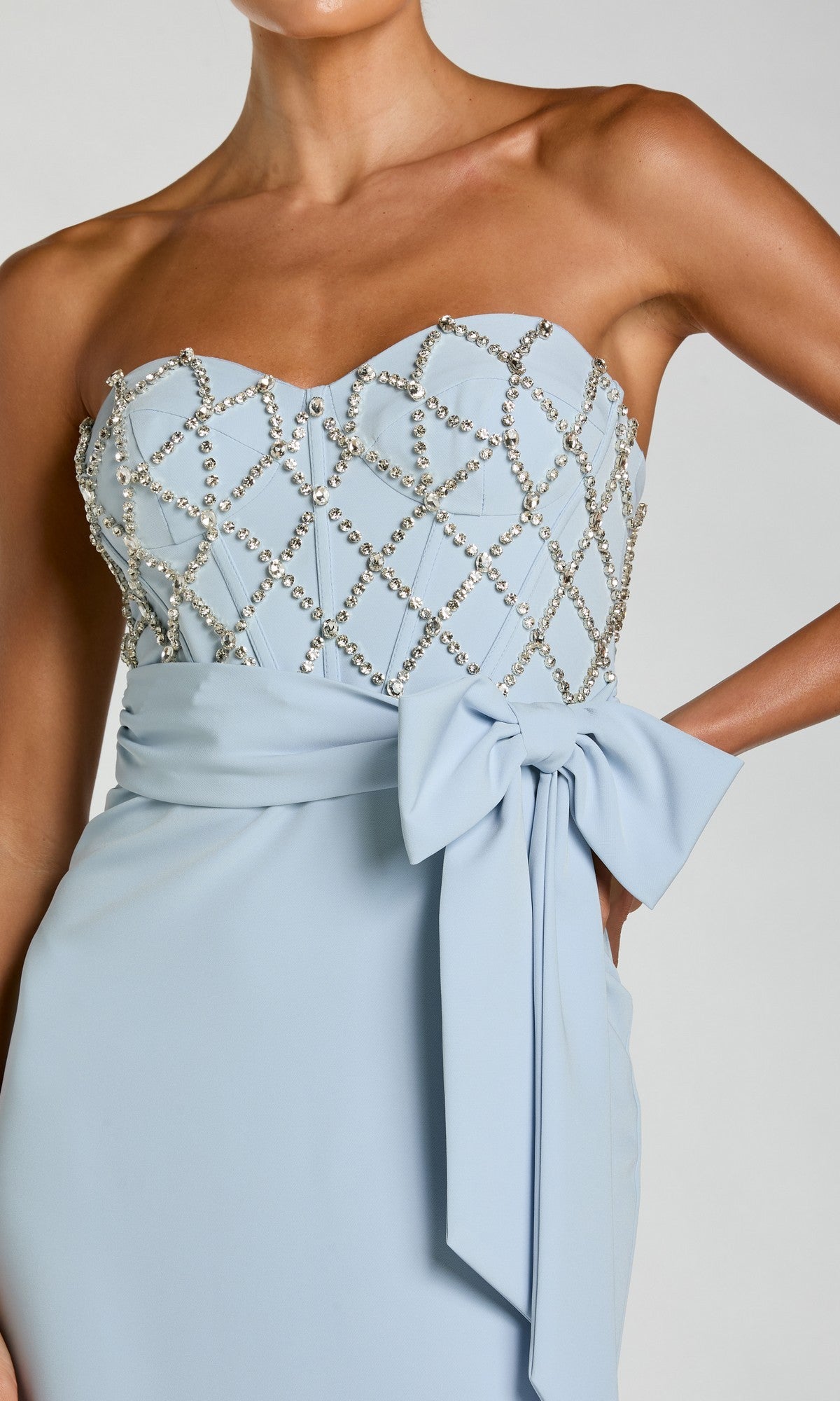 A woman wears the Strapless Sweetheart Formal Gown: Mac Duggal 2294 in light blue, featuring a beaded grid bodice and a large waist bow.