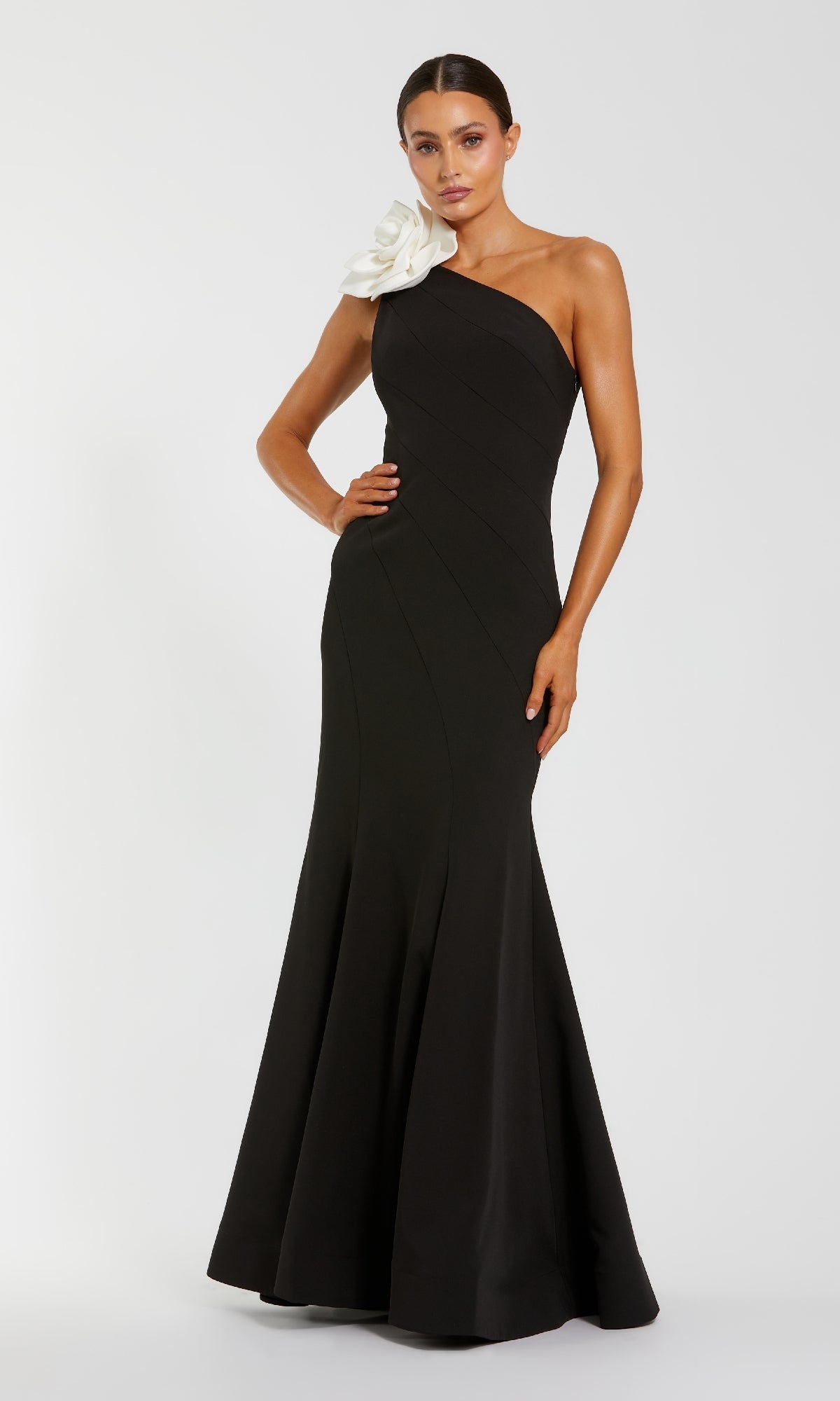 Woman wearing a black one-shoulder gown with a white flower on a white background