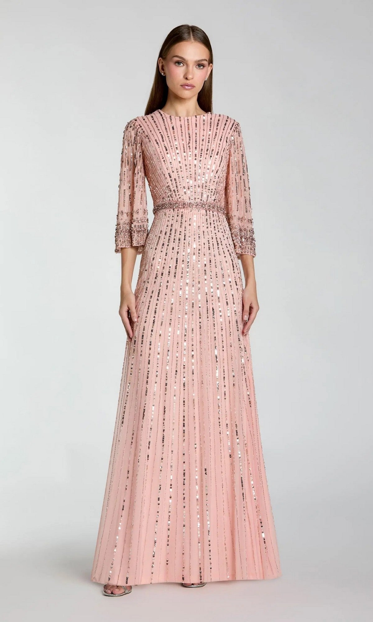 A woman poses against a plain light gray background wearing the Mac Duggal 23045 Long Formal Dress in rose, a floor-length modest evening gown featuring sequin vertical stripes and three-quarter sleeves.