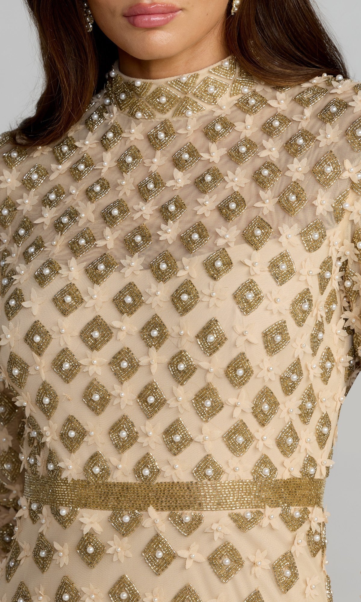 A close-up of a woman wearing the Long Formal Dress: Mac Duggal 23087, showcasing intricate gold diamond-shaped patterns and pearl-like embellishments on sheer nude-gold fabric, epitomizing the gown’s signature elegance.