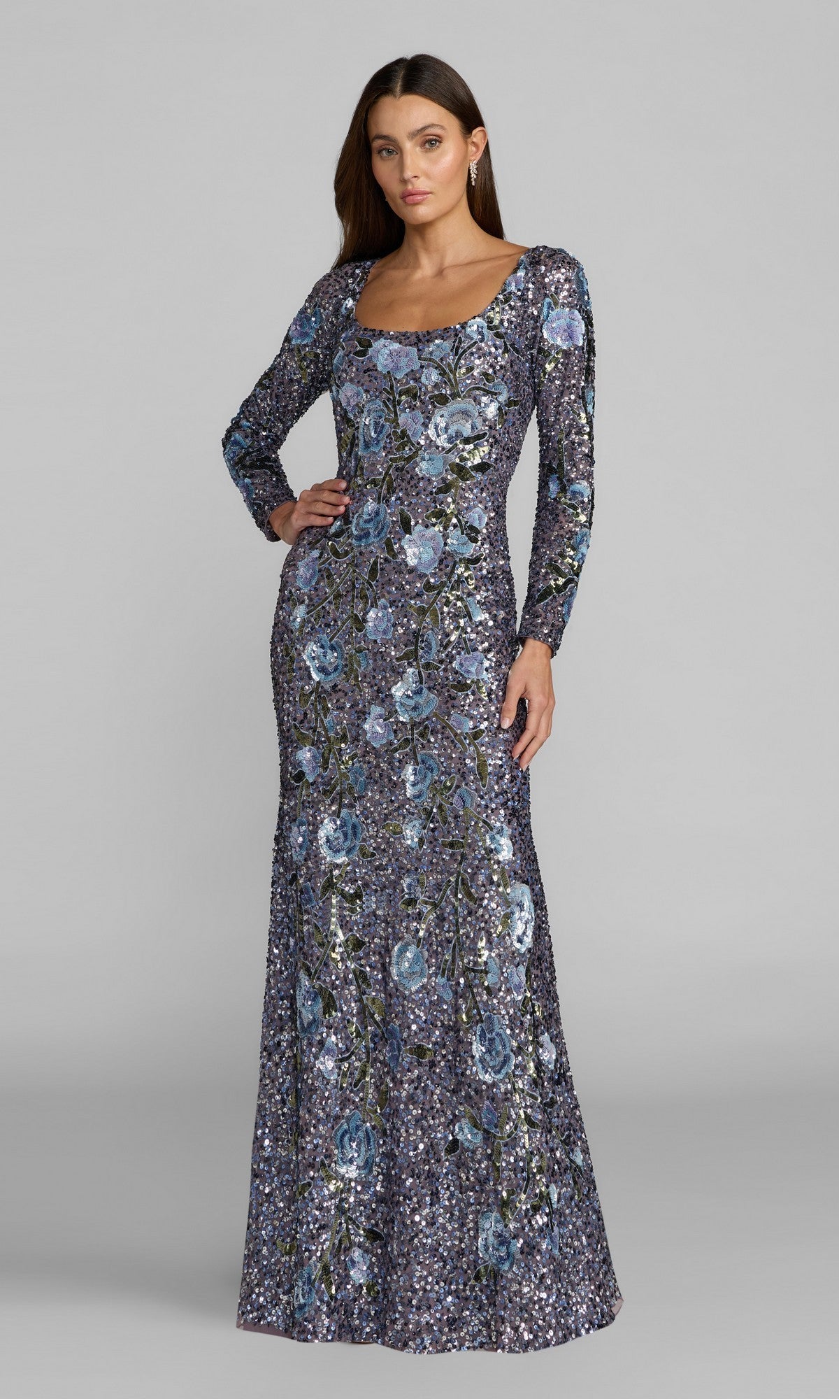A woman wearing the Mac Duggal 23103 Long Formal Dress in Hydrangea Multi, featuring long sleeves and a blue floral sequin design, stands against a plain grey background.