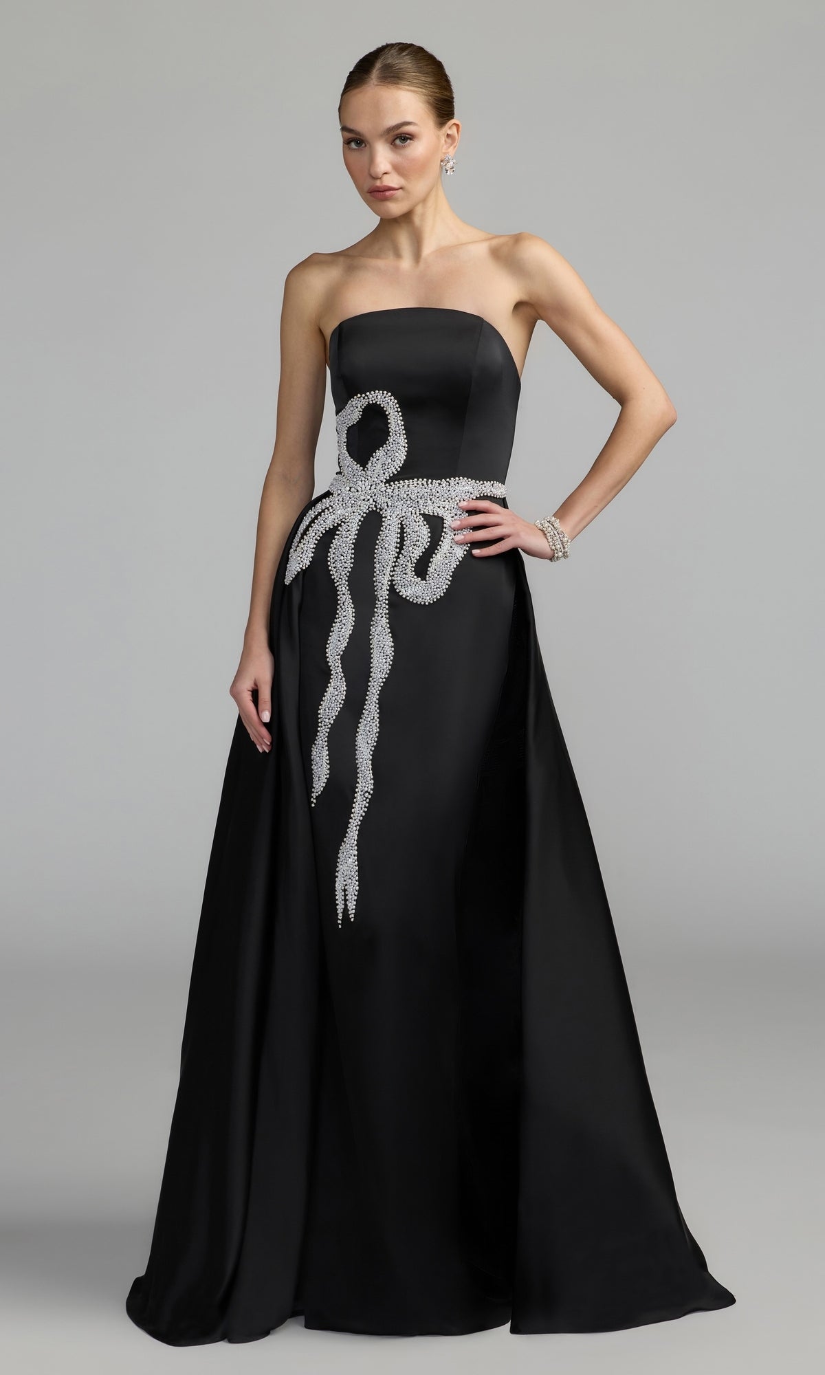 Woman wearing a strapless long formal dress by Mac Duggal (Style 2317), featuring a floor-length black and white gown with a silver jeweled bow design on the bodice and hip, standing against a plain gray background.