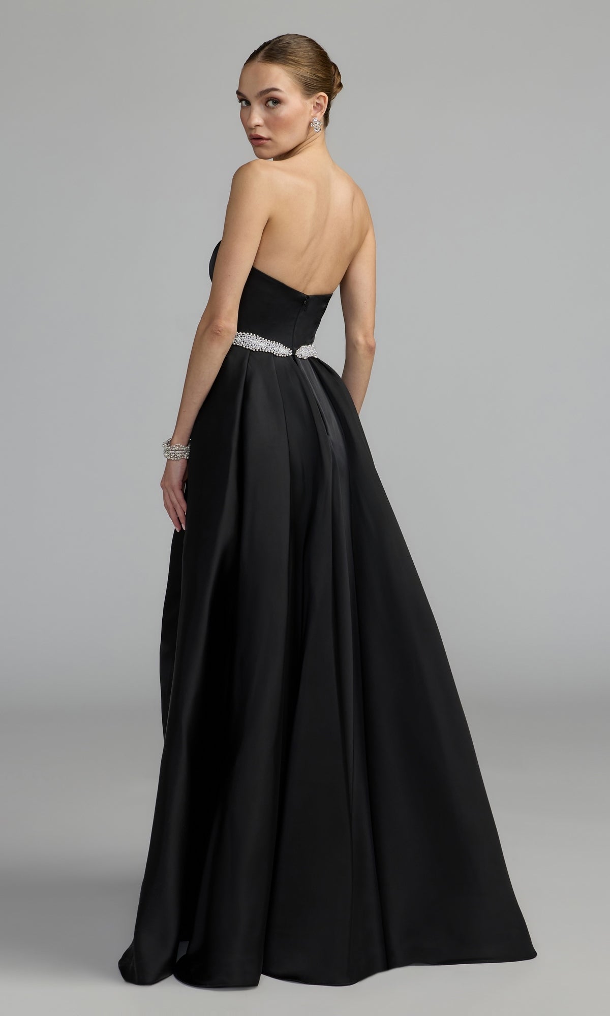 Woman in a strapless long blue formal dress—Mac Duggal 2317—looking over her shoulder against a plain gray background, exuding timeless elegance reminiscent of classic Mac Duggal designs.