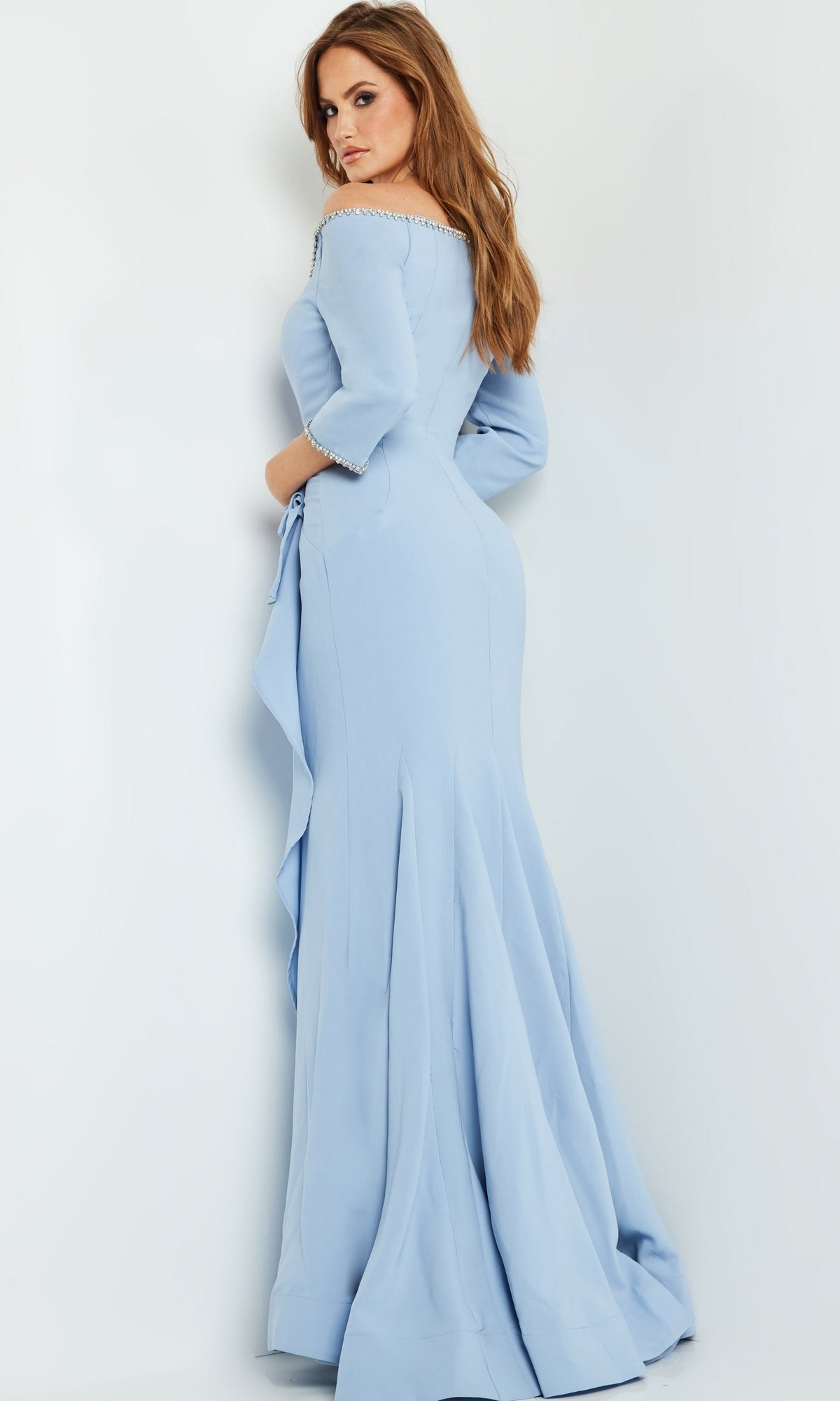 A woman in the Jovani Long Formal Dress with Bead Trim 23190, a light blue off-the-shoulder gown, stands against a white background looking over her shoulder.