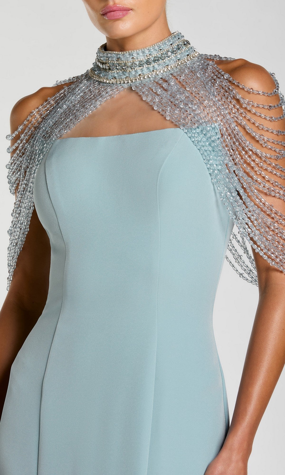 A woman wears the Long Formal Dress: Mac Duggal 2334, a sleeveless light blue gown with a sheer, beaded capelet draped over her shoulders and neck, featuring an elegant beaded halter collar reminiscent of classic Mac Duggal mermaid formal gowns.