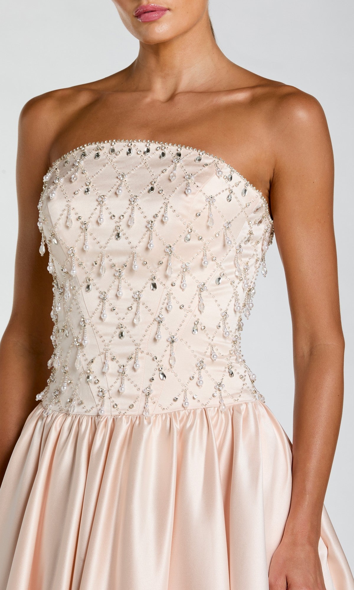 A woman wearing the Mac Duggal 2354 long formal dress, a strapless satin gown in light pink with a fitted, beaded bodice and a flared skirt.