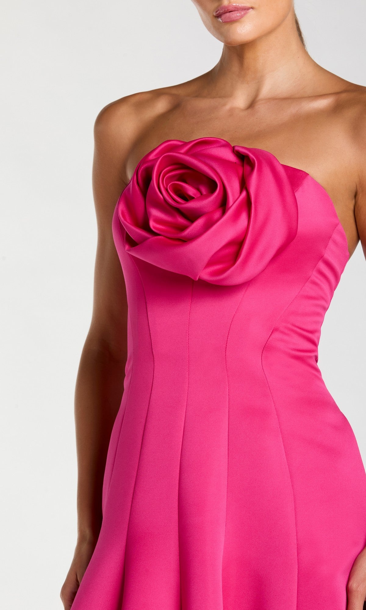 A woman wearing the Mac Duggal 2357, a long formal strapless, fitted hot pink crepe-satin dress featuring a large, sculpted fabric rose detail on the chest.