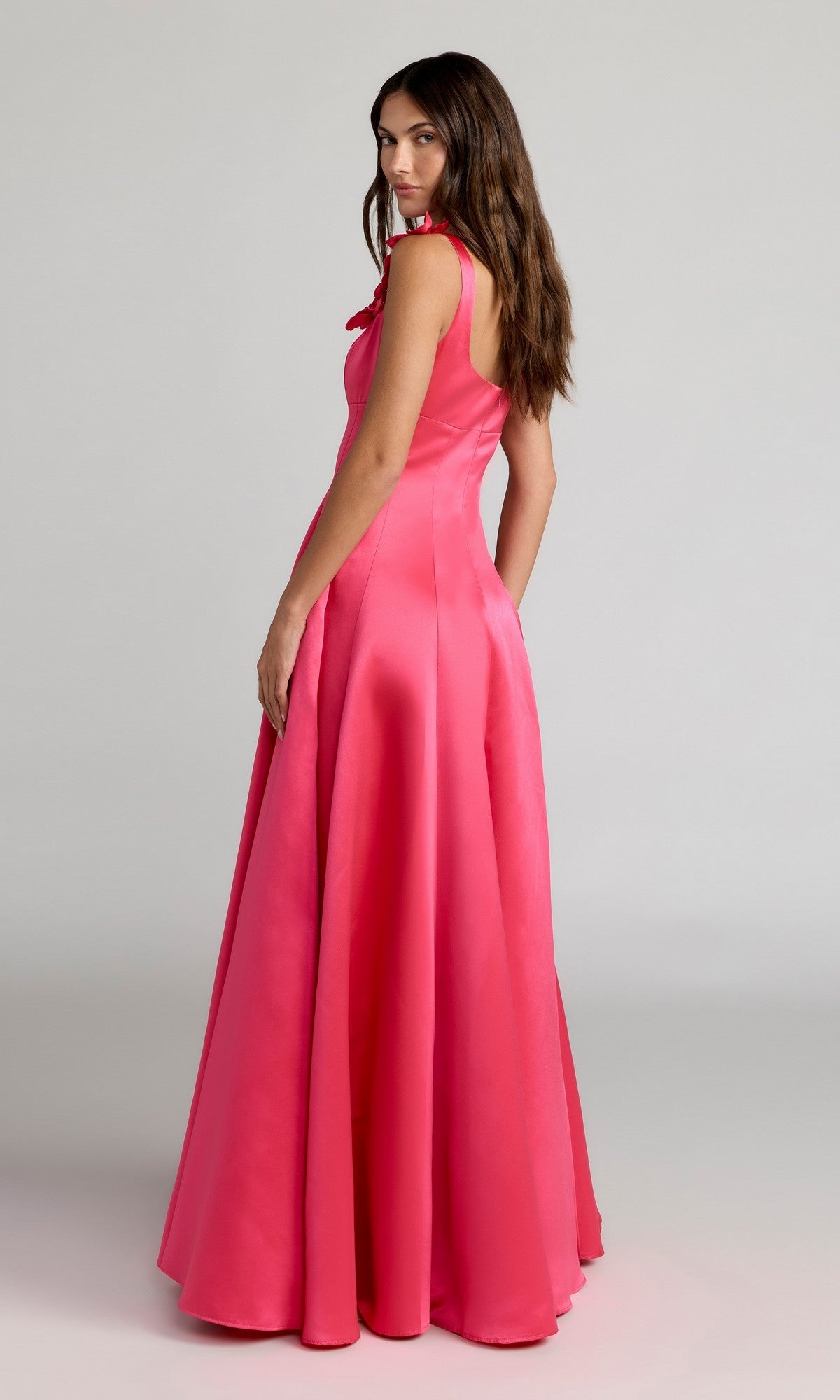 A woman stands in profile against a plain light background, wearing the Mac Duggal 2359—a floor-length, sleeveless hot-pink satin formal gown.