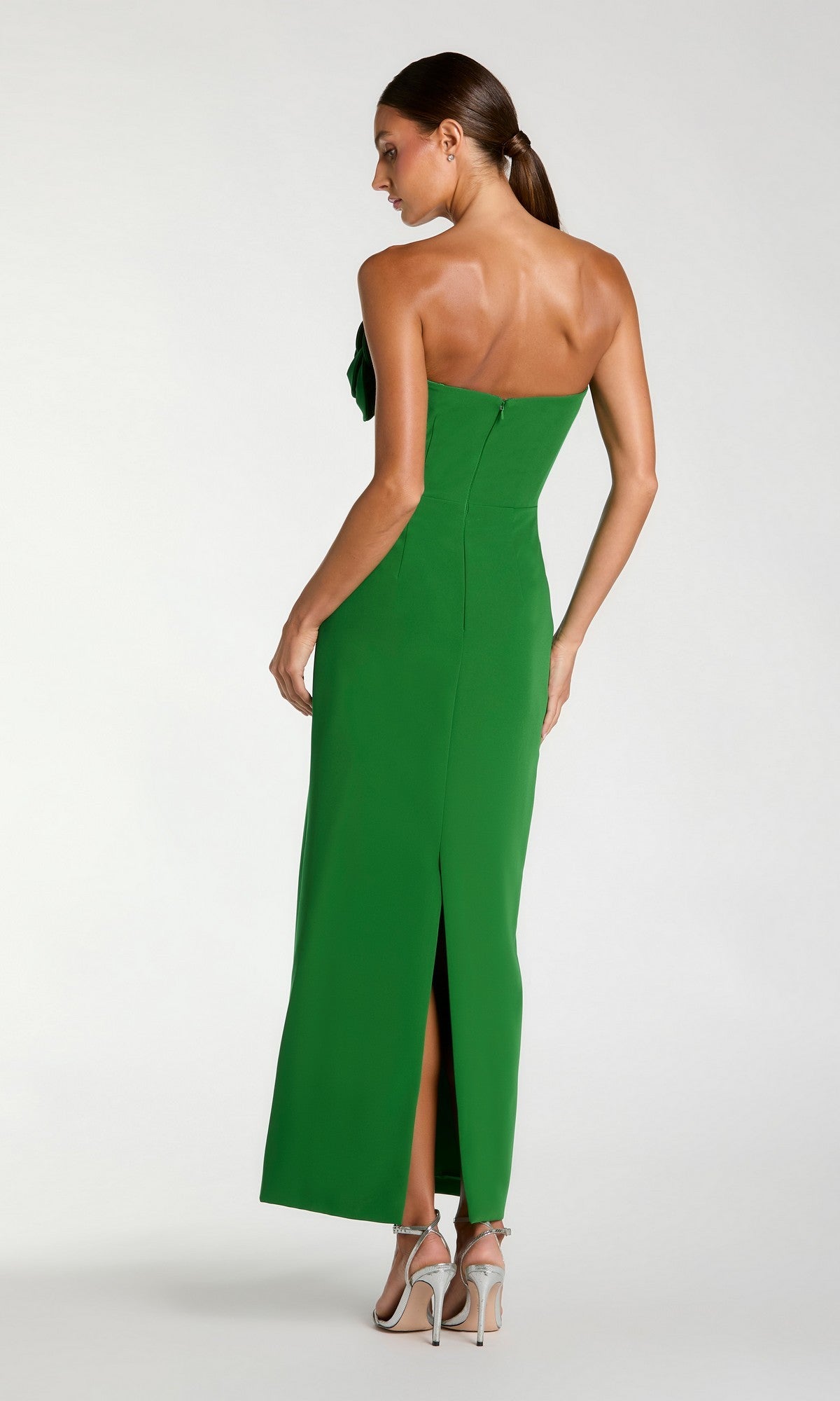 A woman models the Mac Duggal 2361 Long Formal Dress, a strapless crepe midi style featuring a back slit and delicate 3D floral appliques. She poses in high heels, glancing over her shoulder against a plain background.