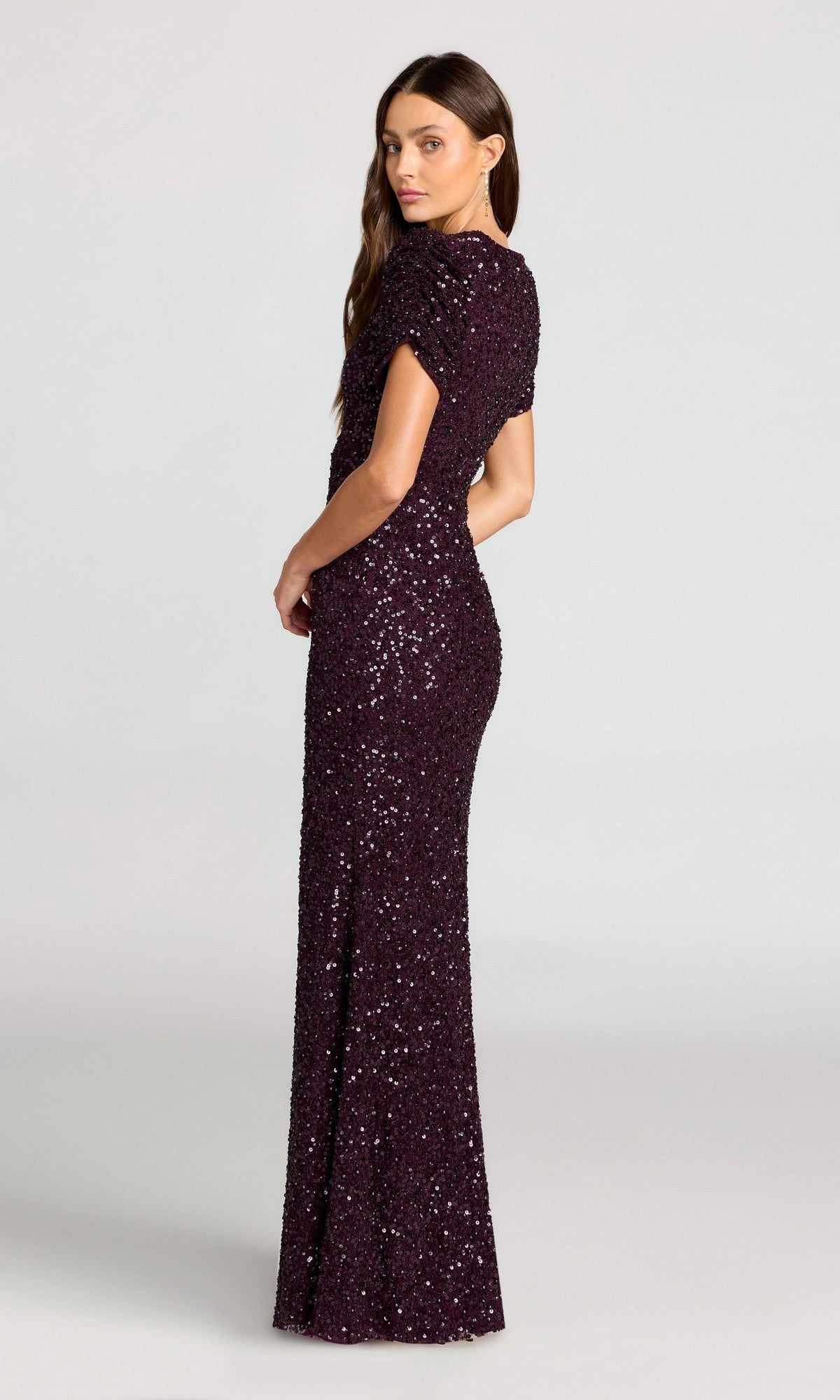 A woman models the Mac Duggal 24003 Short Sleeve Sequin Formal Dress, standing sideways and looking over her shoulder against a plain light background.
