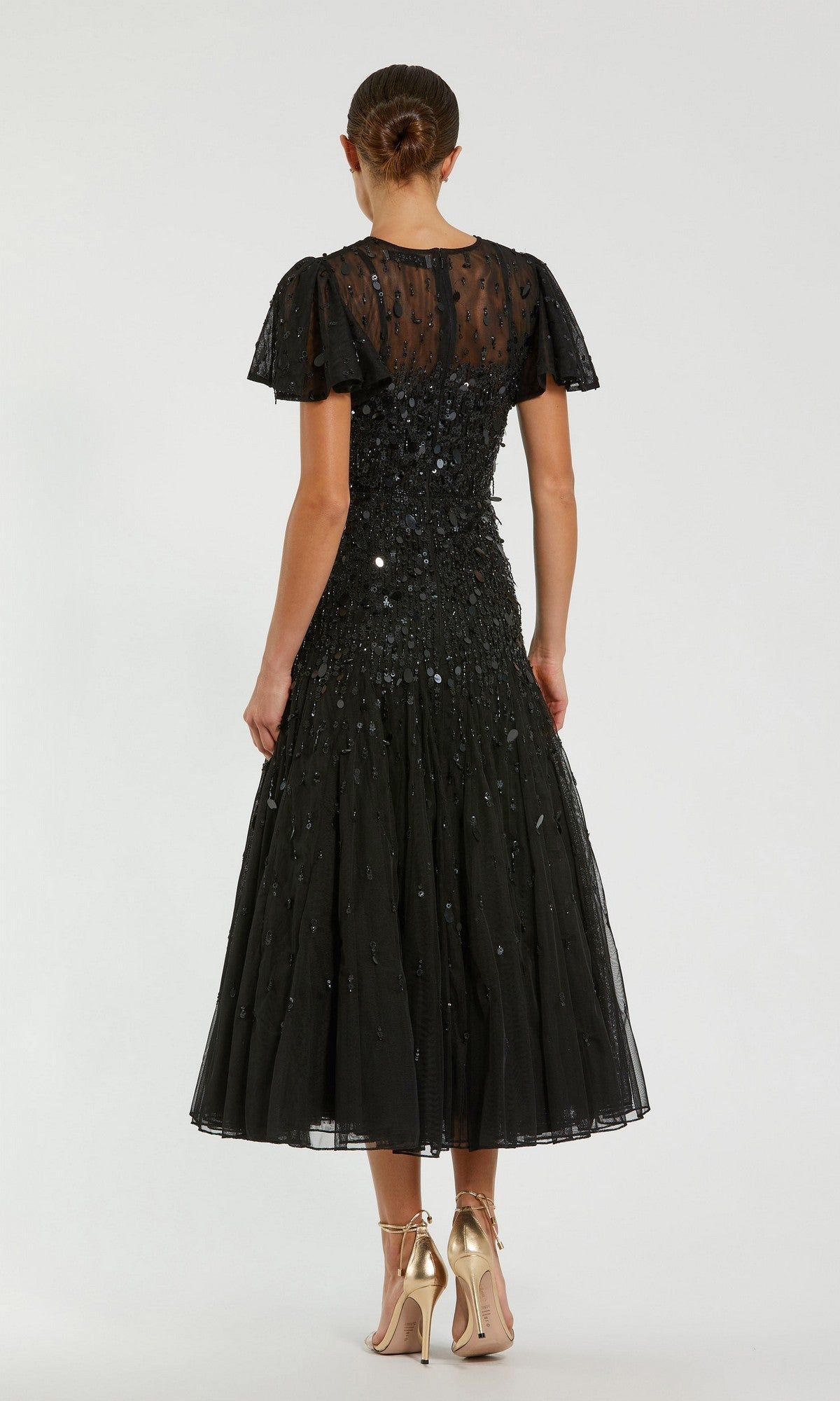 A woman faces away, wearing the Mac Duggal 24018 Brown Tea-Length Party Dress—a semi-formal party dress—paired with gold high heels.
