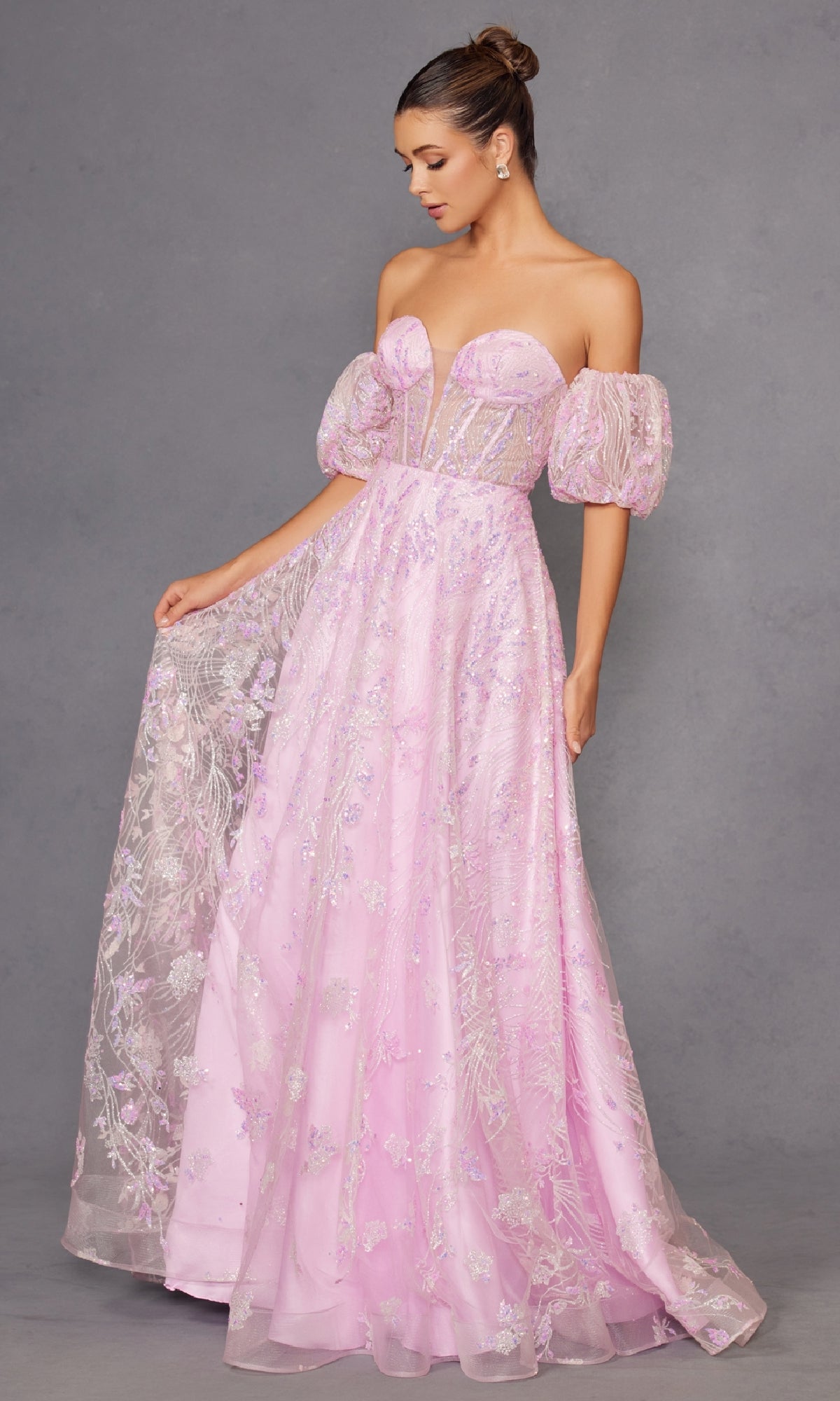 A woman models the Puff-Sleeve Strapless Long Glitter Prom Dress 2404 in pink, featuring puffed sleeves and floral details, standing against a gray background while holding part of her skirt to the side.