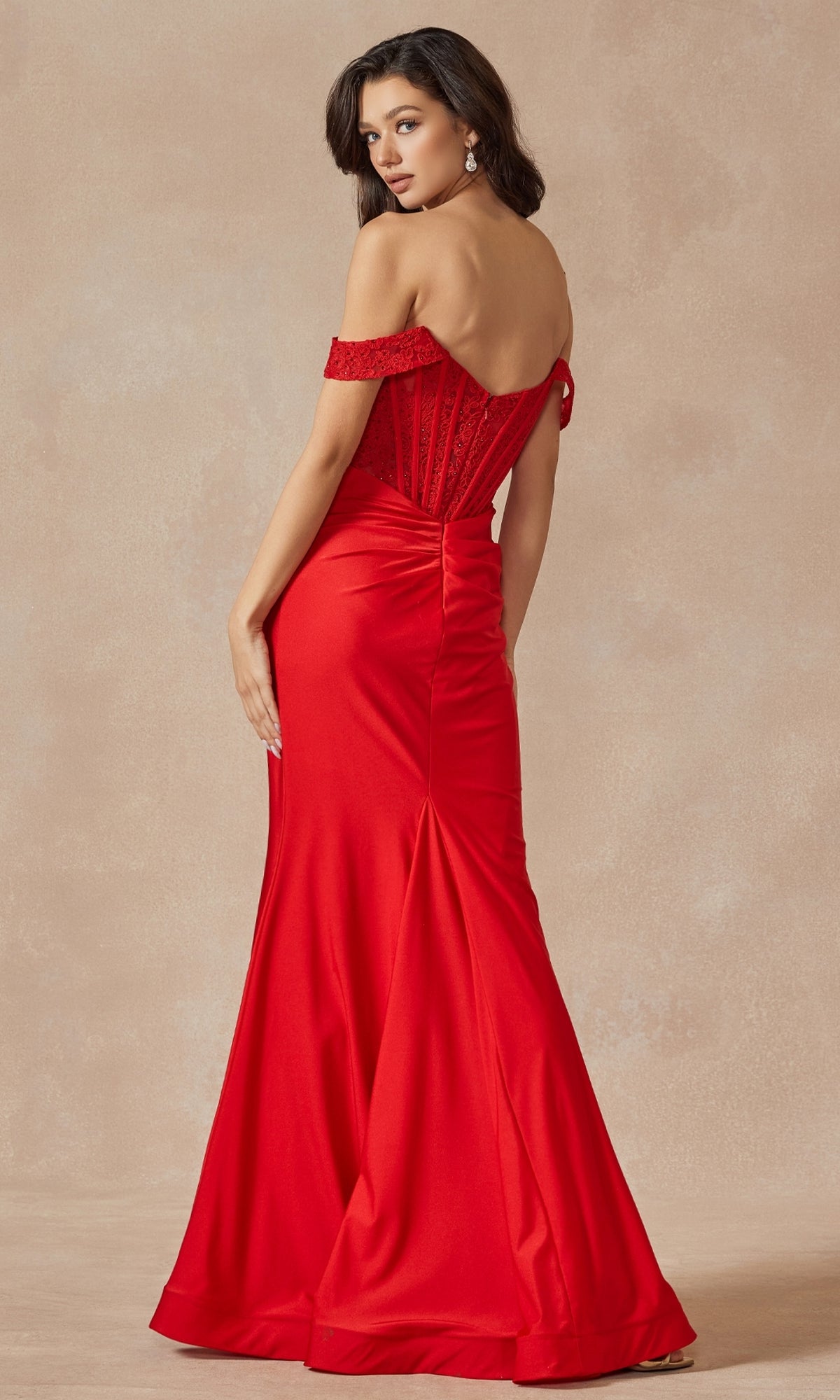 A woman in the Lace-Bodice Off-the-Shoulder Long Prom Dress 2407, featuring a bright red hue, lace corset bodice, and slight train, stands facing backward and looks over her shoulder.