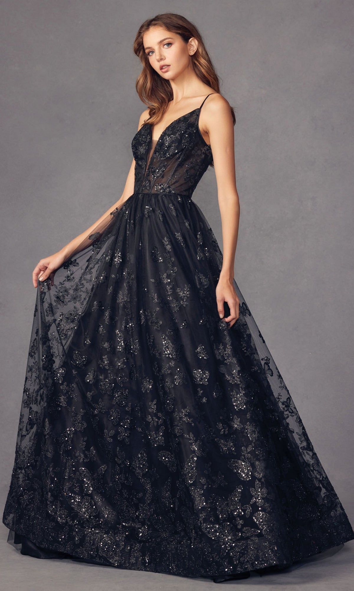 A woman wears the Sheer-Corset Glitter-Print Long Prom Dress 2413, featuring a sleeveless design, sheer bodice, black glitter floral patterns, and an elegant floor-length a-line tulle skirt.