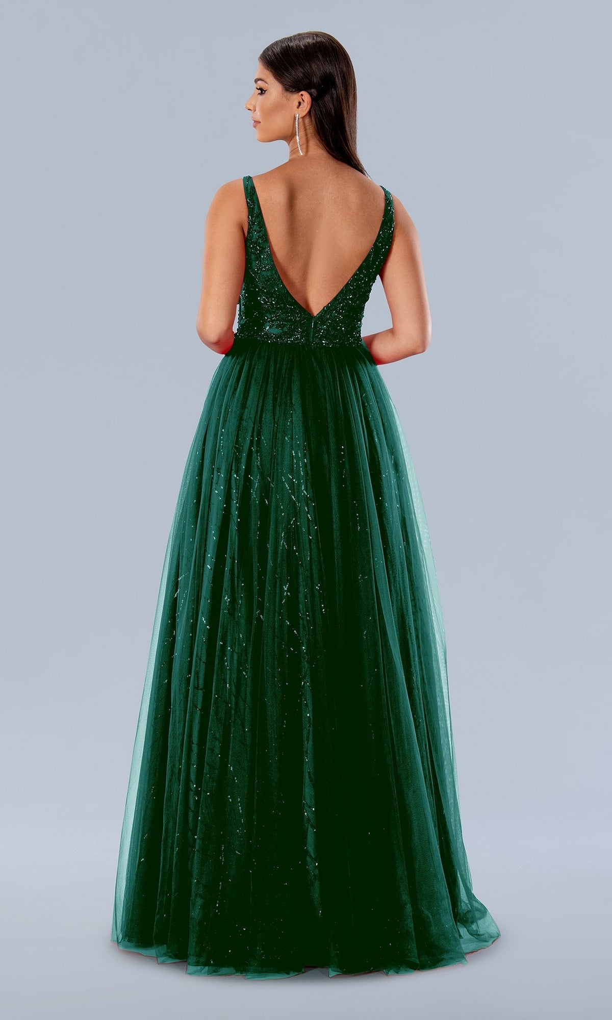 Woman wearing the Stella Couture 24150 V-Neck Long Tulle Prom Dress, a sleeveless floor-length emerald gown with a deep V-back, standing against a plain light background.