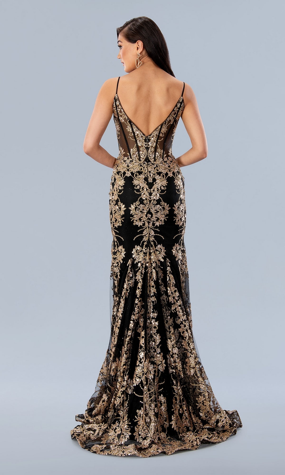 A woman faces away, wearing the Long Prom Dress 24159 by Stella Couture—a black mermaid formal gown with metallic gold floral embroidery and a deep V-back.