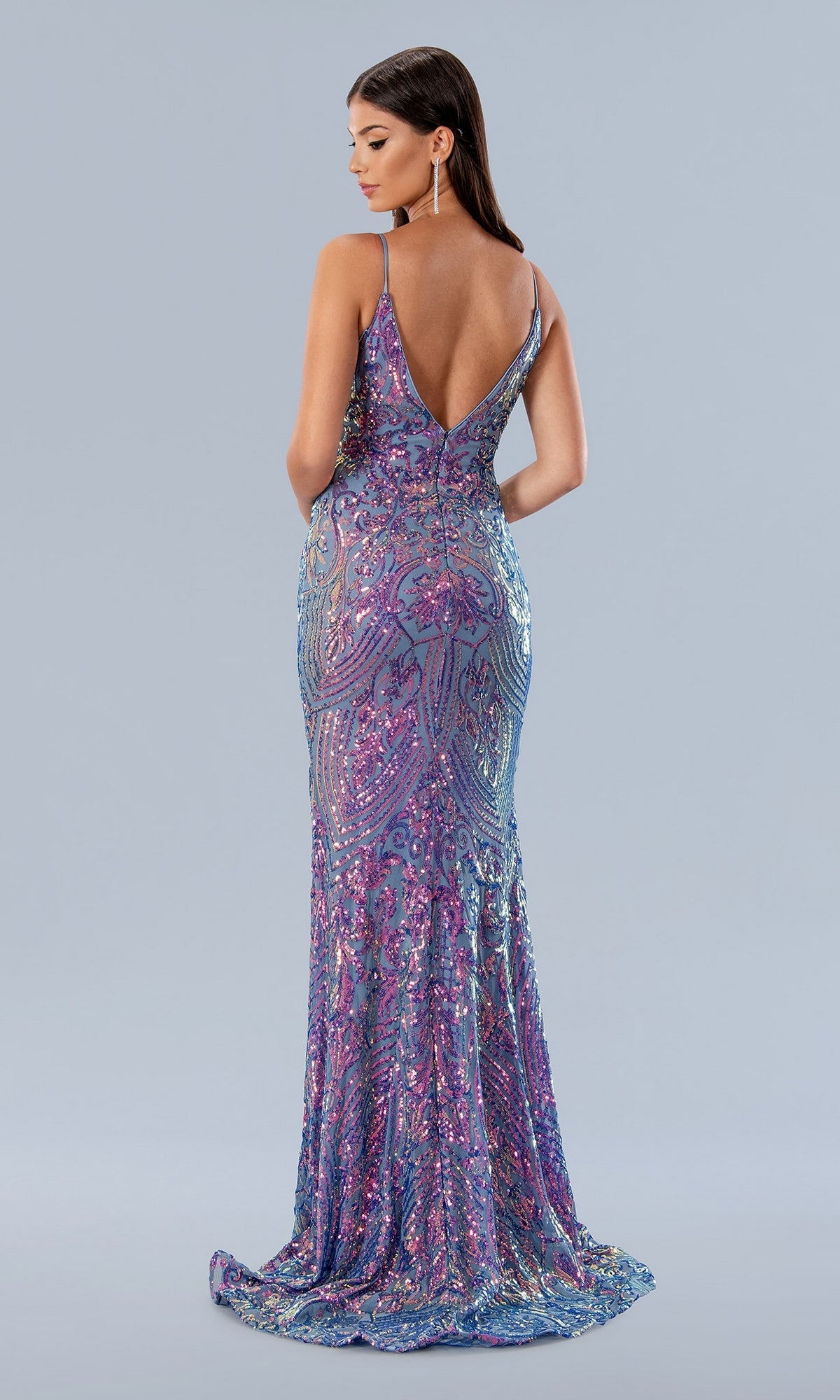 Woman wearing the Long Prom Dress 24160 by Stella Couture—a fitted, floor-length purple sequin mermaid gown with a deep V-neckline and open back—stands facing away against a plain light gray background.