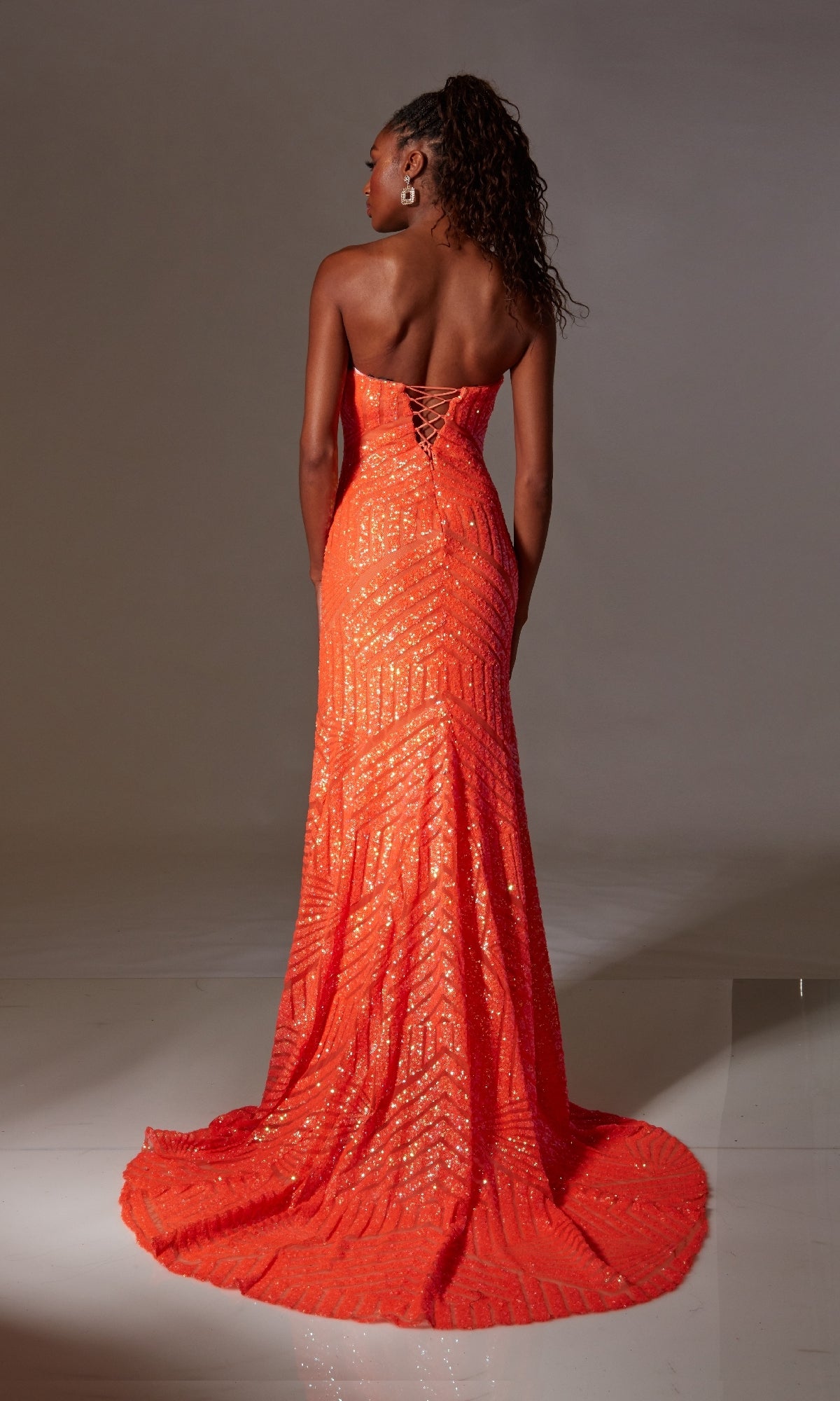 A woman in the Strapless Long Sequin Prom Gown: Aerie Couture 243, featuring a lace-up back, stands facing away against a plain background.