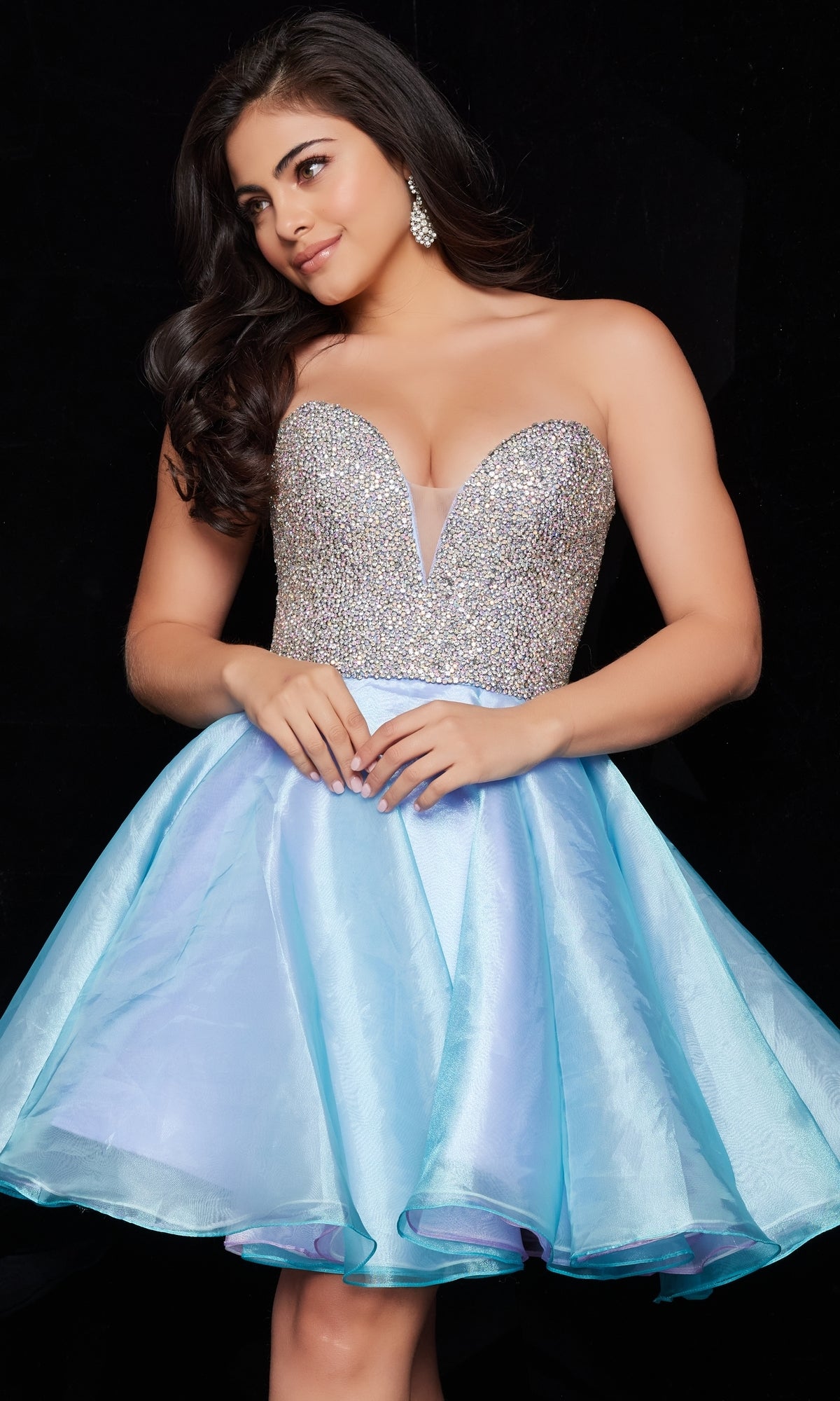 A woman stands against a black background wearing the Jovani Strapless Blue Short Party Dress 24547, featuring a beaded silver-sequined bodice and a flared satin skirt.