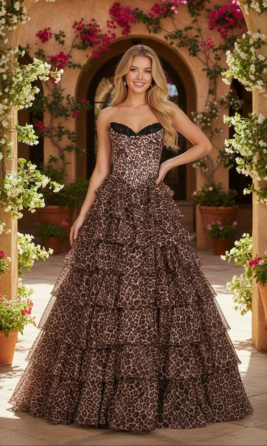 Outdoors, a woman wears the Long Prom Dress: PromGirl Exclusive 250123A—a strapless ball gown with a sweetheart neckline and tiered leopard print. Flowers and greenery frame the background.