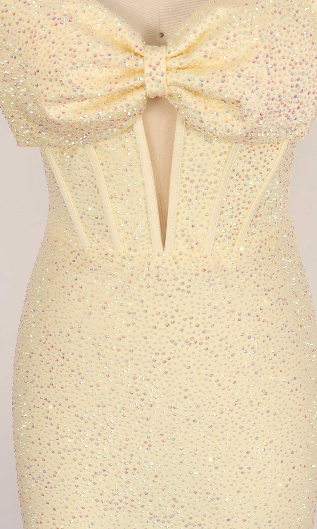 Close-up of the PromGirl Exclusive 250142 homecoming dress, a light yellow strapless design adorned with dazzling rhinestones, featuring a large bow on the bodice, sheer mesh panel, and structured corset-style seams.