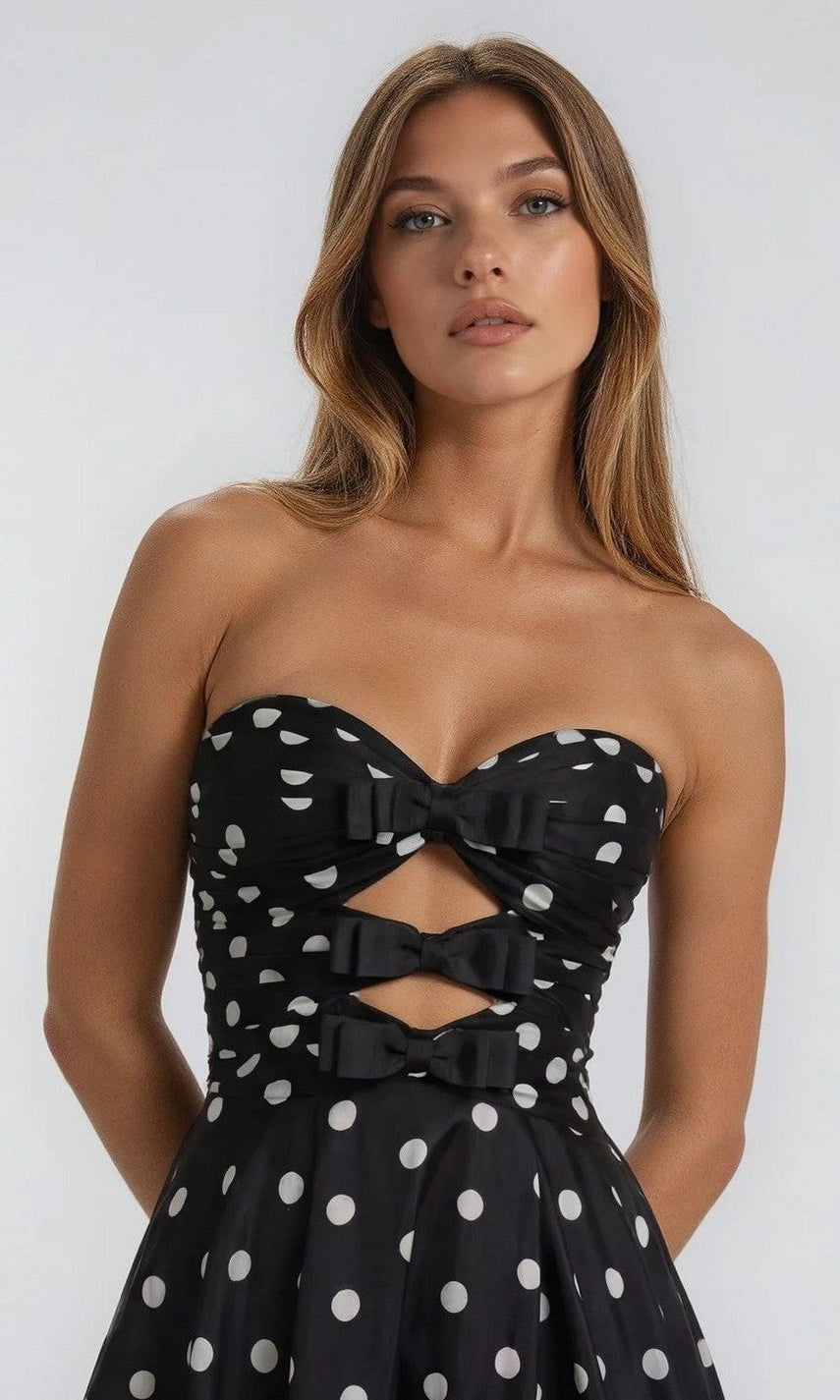 A woman wears the Polka-Dot Long Prom Dress: PromGirl Exclusive 250209, a strapless prom dress with white polka dots, chic cut-outs on the bodice, and bow details for a stylish vintage vibe.