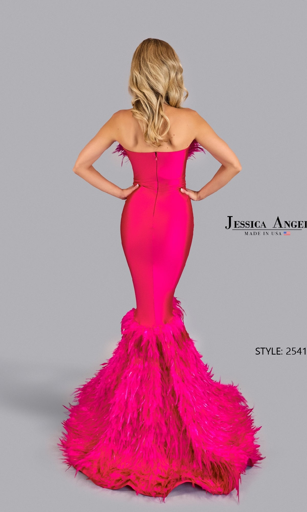 A woman wearing the Jessica Angel 2541 Mermaid Prom Dress with Feathers in hot pink, strapless and fitted with feather detailing at the hem and back, stands against a plain gray background, facing away from the camera.