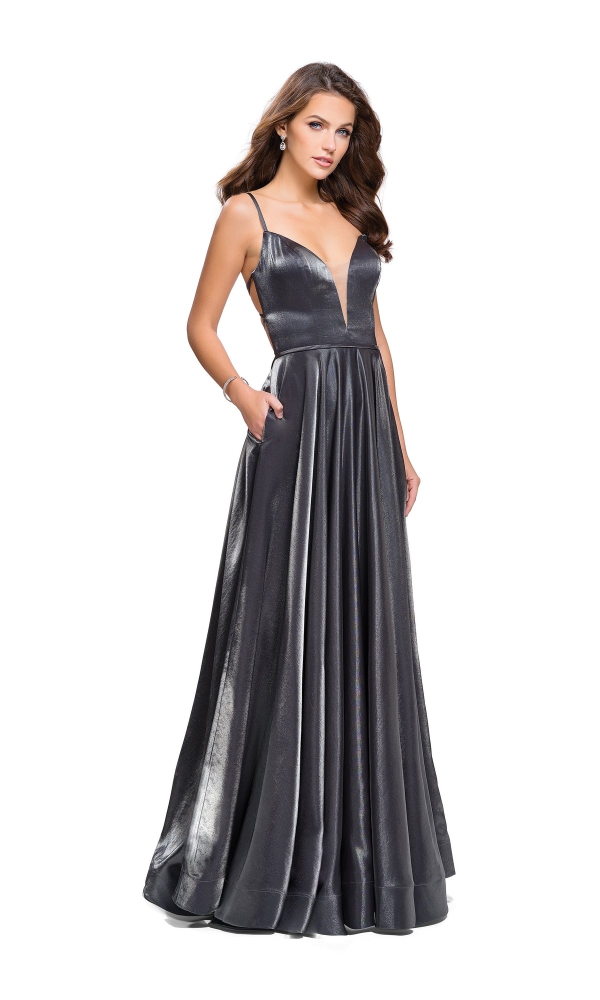 A woman wears the La Femme 25670 Long Prom Dress, a sleeveless metallic gray gown with a deep V-neckline, open back, and floor-length hem, posing with hands in pockets against a white background.