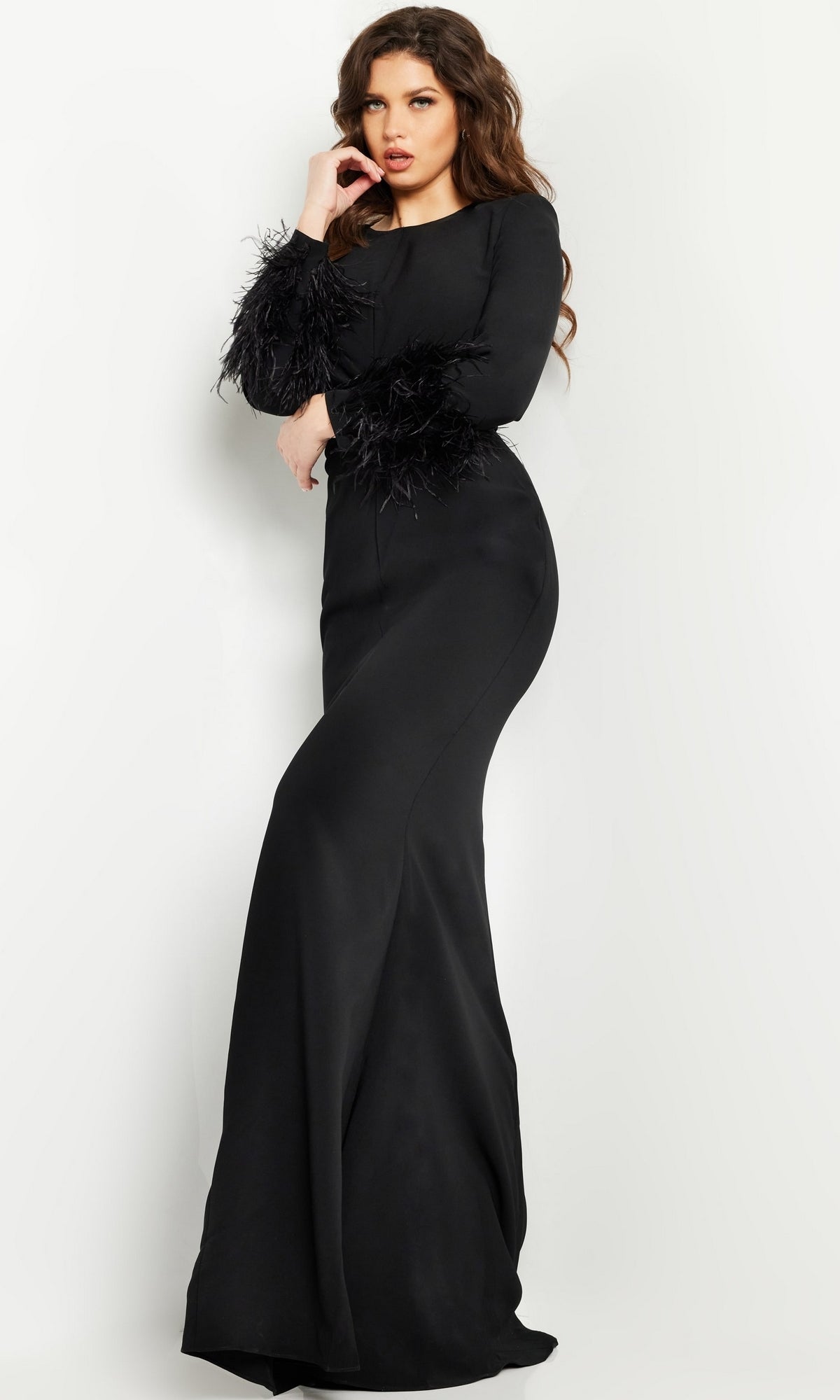 A woman stands against a white background wearing the Jovani Long Sleeve Long Black Formal Dress 25898, featuring elegant feathered cuffs.