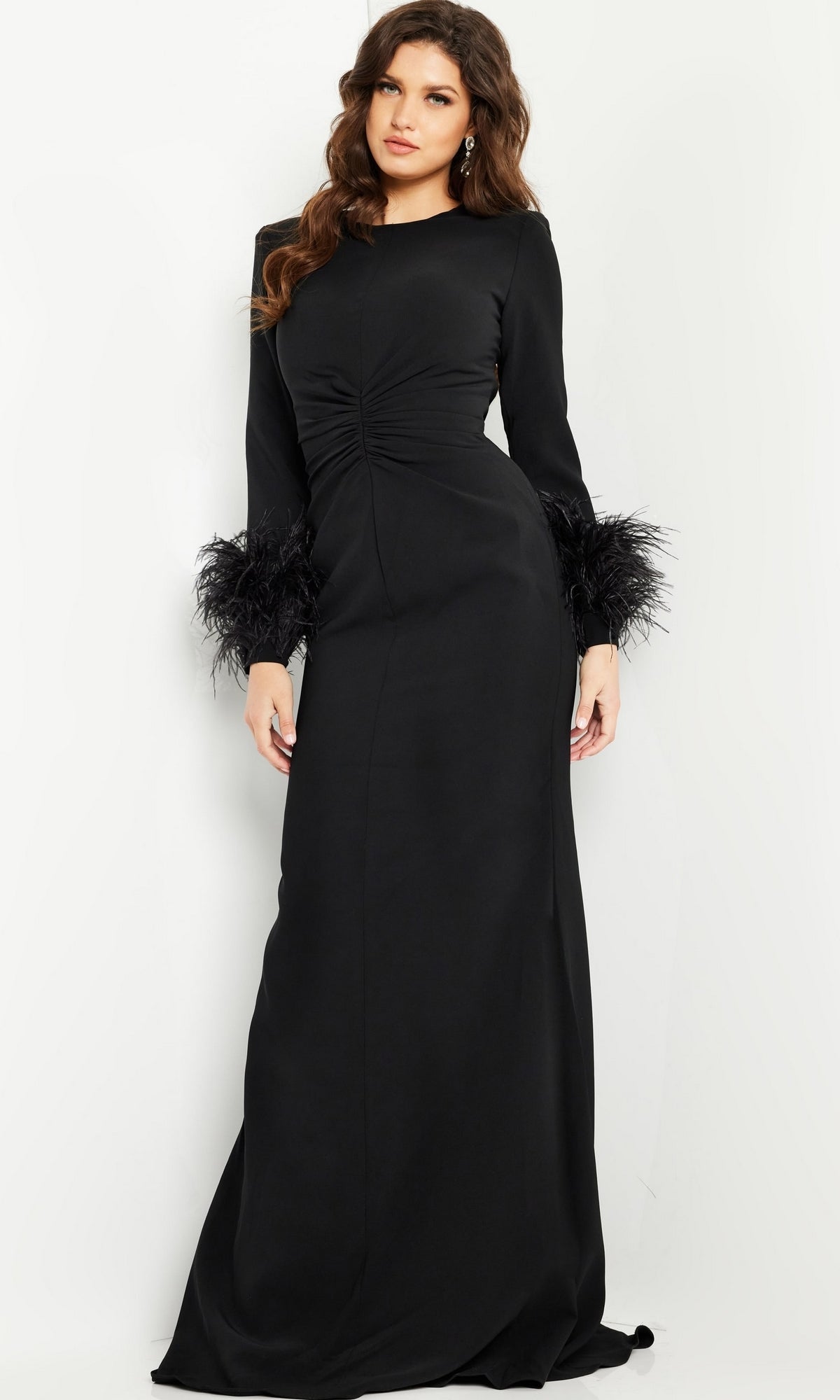 A woman models the Jovani Long Sleeve Long Black Formal Dress 25898, featuring ruched waist detailing and feathered cuffs, against a plain light background.