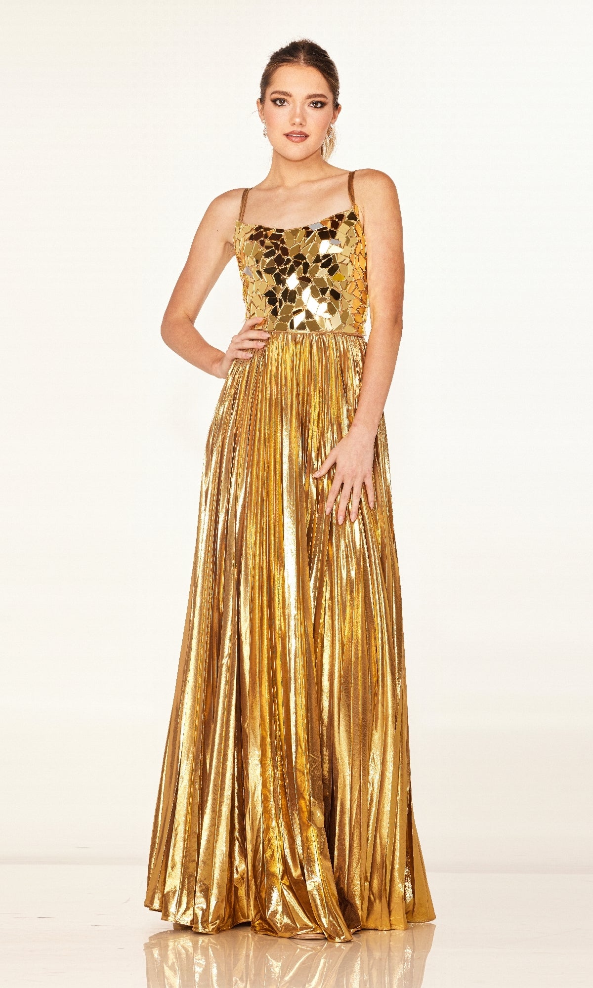 A person stands wearing the Long Prom Dress: Cecilia Couture 2609, a shiny gold gown with a fitted, embellished bodice featuring reflective mosaic-like pieces and thin straps.