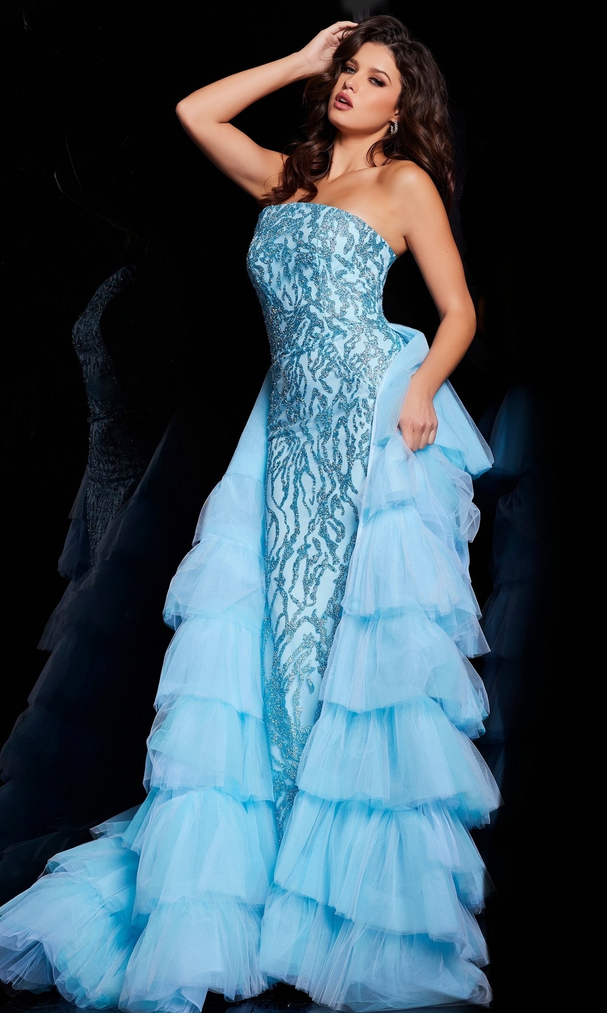 A woman poses against a black background in the Jovani Ruffled Long Glitter-Print Prom Dress 26119, featuring sparkling patterns and tiered ruffles that highlight the gown’s elegant, glamorous style.