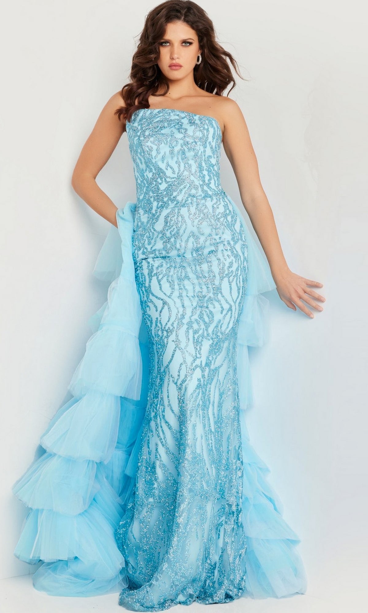 A woman poses in the Jovani Ruffled Long Glitter-Print Prom Dress 26119—an elegant strapless, fitted light blue gown with a tiered tulle train, ideal for your next formal event.