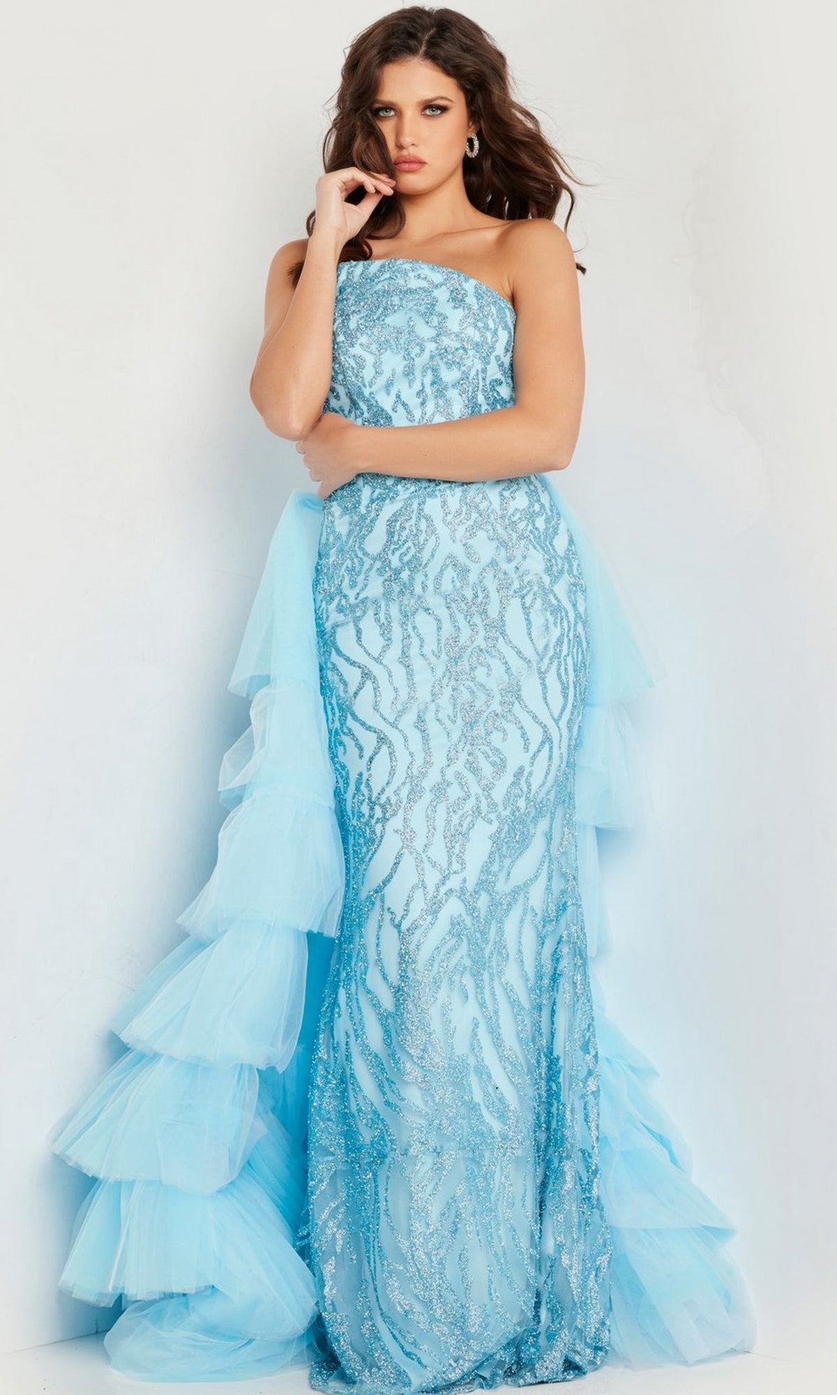A woman stands against a white background wearing the Jovani Ruffled Long Glitter-Print Prom Dress 26119, featuring sequin patterns, a strapless neckline, and layered tulle ruffles on one side.