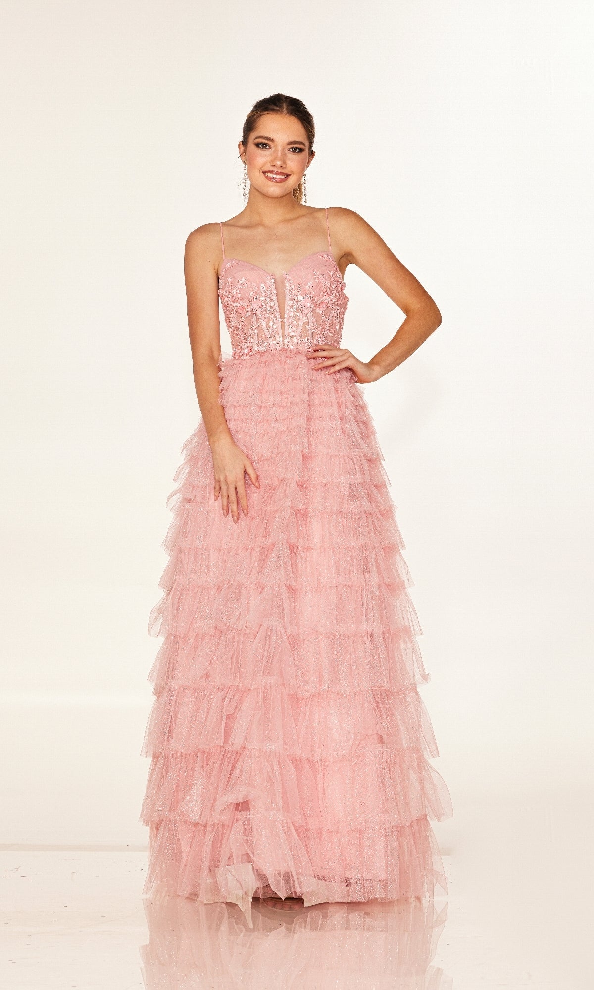 A woman smiles in the Cecilia Couture 2613 long prom dress—pink, tiered tulle with thin straps and a fitted, embroidered corset bodice—against a plain white background.