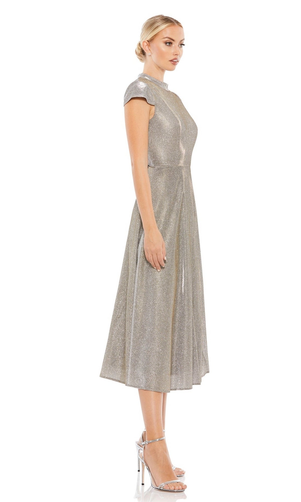 A woman in profile wears the Short Wedding Guest Dress 26151 by Mac Duggal, a silver metallic dress with cap sleeves and a subtle shimmer, styled with metallic heels, against a plain white background.