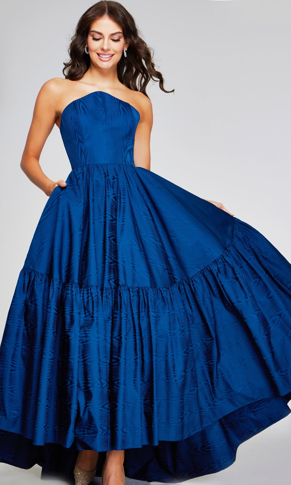 A woman models the Long Formal Dress: Jovani 26152— a royal blue strapless taffeta gown with a fitted bodice and full, tiered skirt—standing against a light gray background.