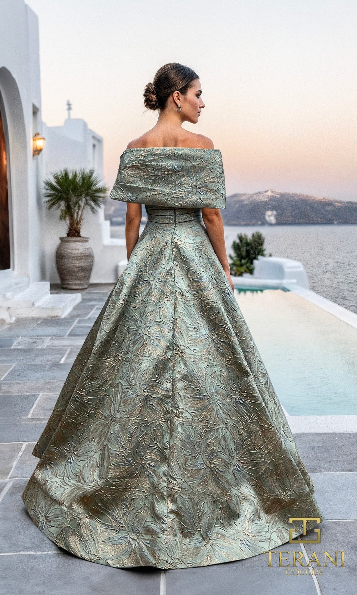 A woman in a Long Formal Dress: Terani 261M6453 stands by a pool, facing away, with white buildings and water in the background.