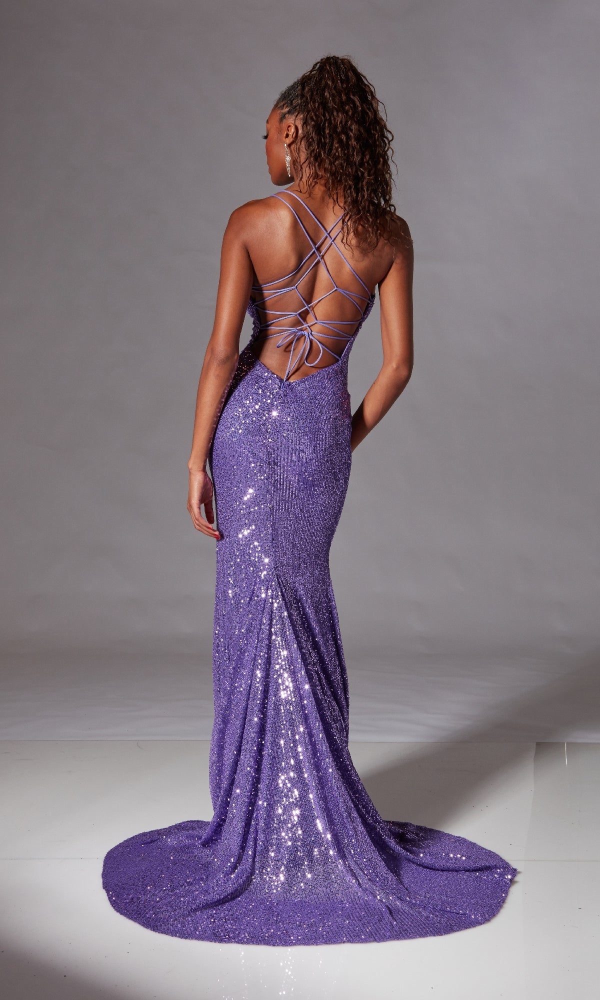 Model showcases the Strappy Long Sequin Prom Dress: Aerie Couture 261, a floor-length purple gown with a strappy-back design, standing on a white floor against a neutral backdrop.