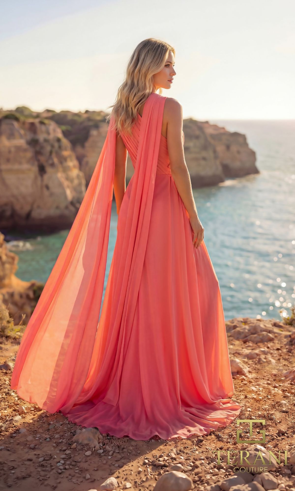 A woman in a Terani 261E6205 long formal dress stands on a rocky cliff overlooking the ocean, sunlight highlighting her hair and her elegant floor-length gown.
