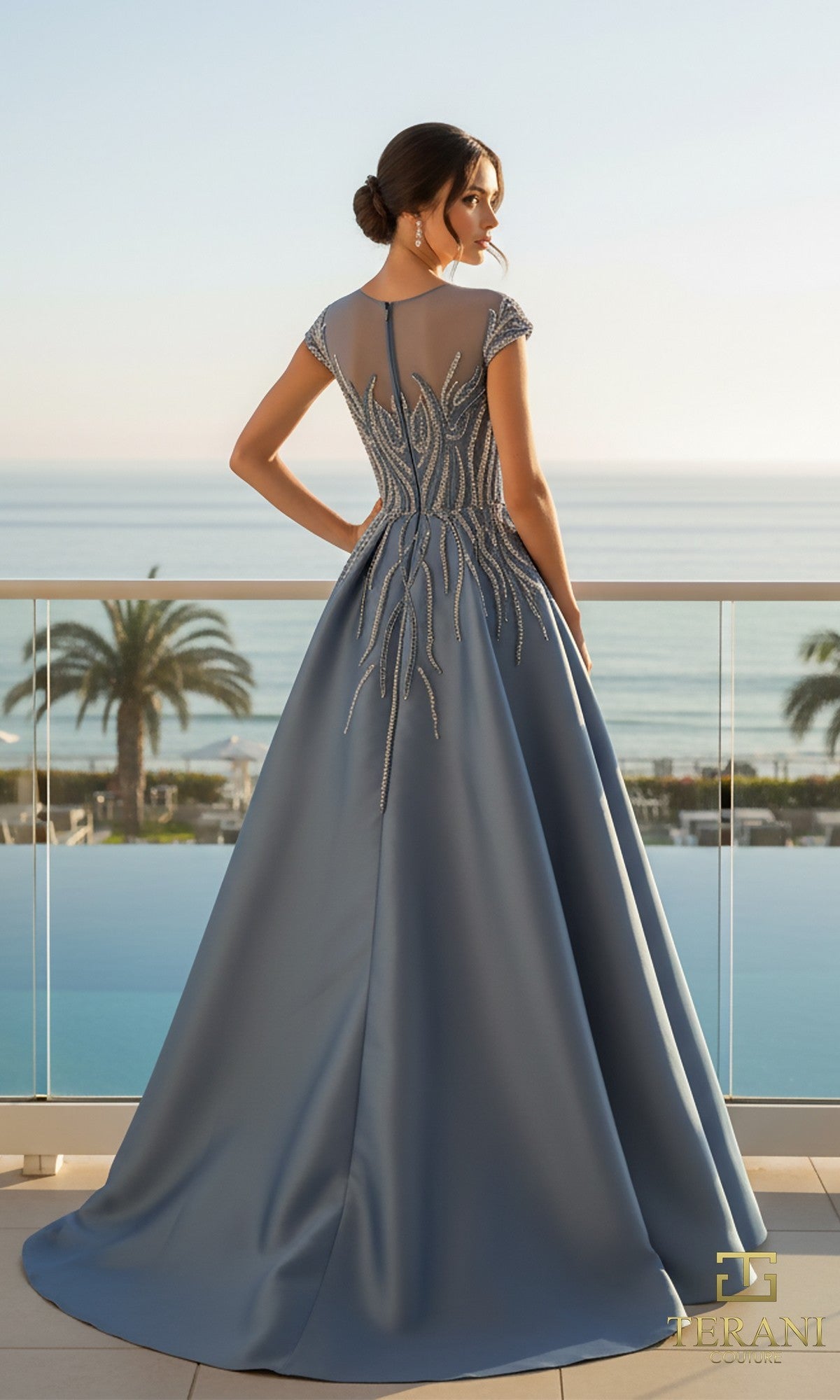 A woman in the Terani 261E6254 long formal dress, featuring stretch Mikado and beaded details, stands on a balcony overlooking the ocean and palm trees.