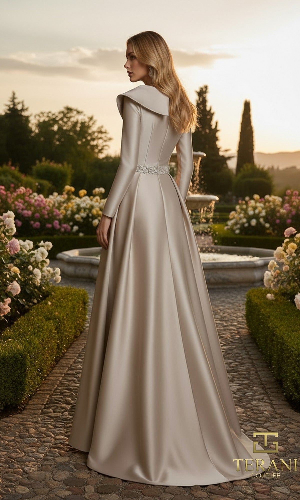 A woman in the Terani 261M6455 long formal dress stands on a cobblestone path outdoors, surrounded by gardens and a water fountain.